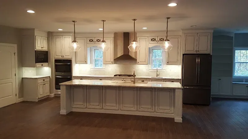 A spacious kitchen featuring white cabinets, a large central island with pendant lighting, and dark stainless appliances.