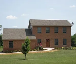 A two-story brick house with a gabled roof and a smaller attached single-story section, set in a grassy yard.