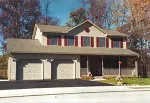 A beige, two-story house with a two-car garage, front porch, and red shutters, surrounded by autumn trees.