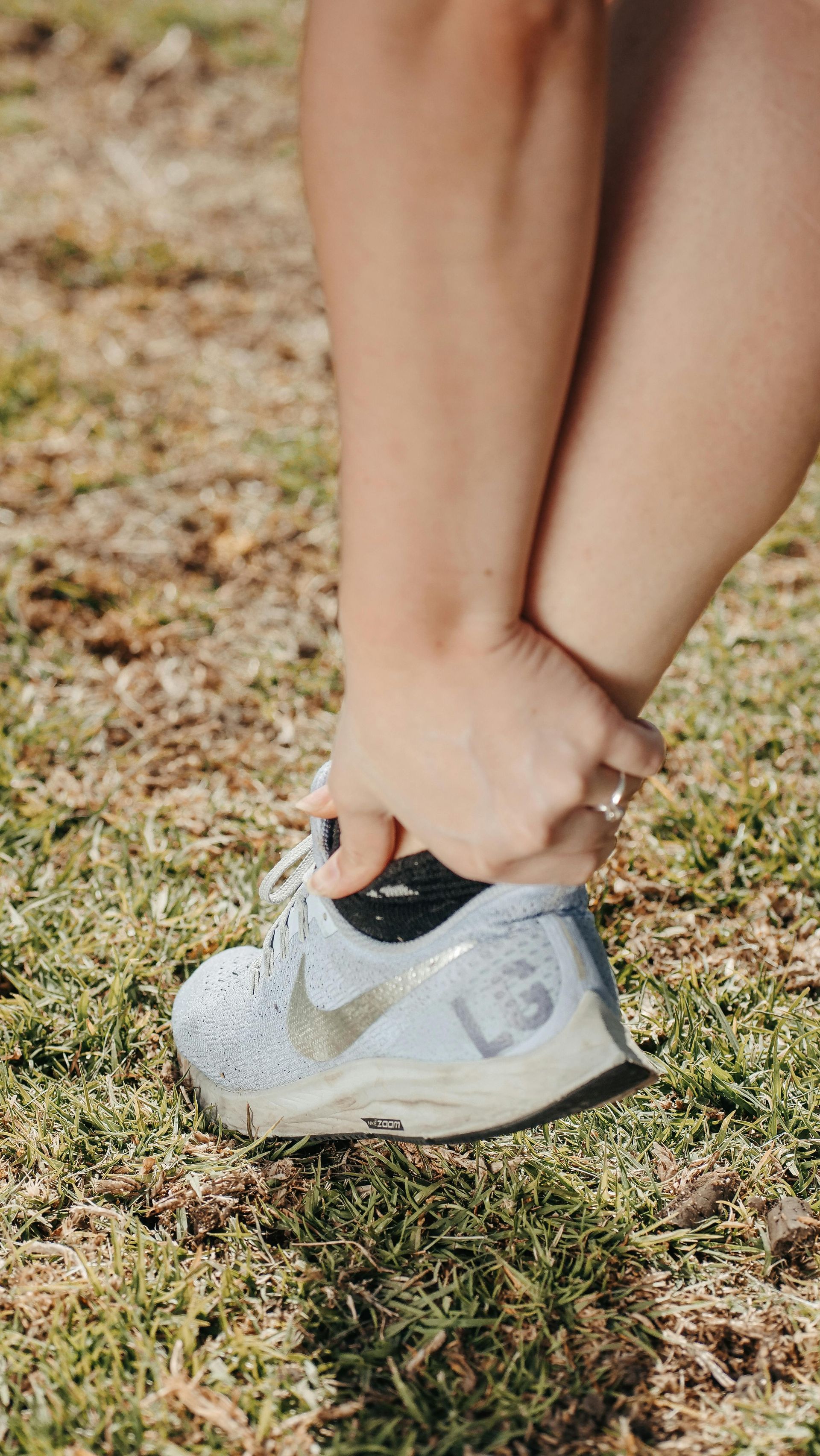 Hands tying the laces of a white running shoe on grass.