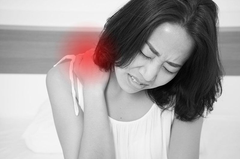 Woman holding her shoulder with a red highlight, showing pain or injury