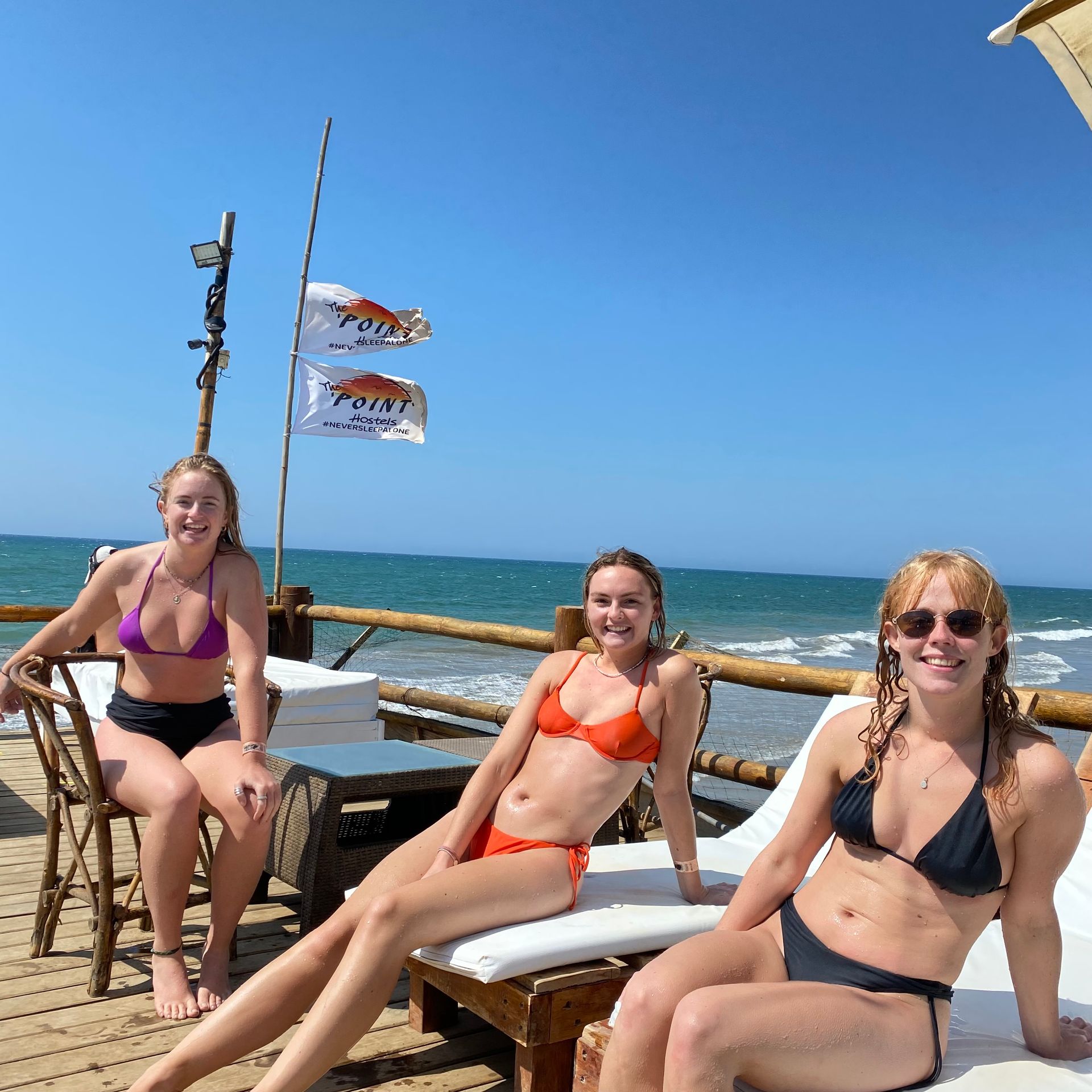 Three women in bikinis are sitting on chairs near the ocean