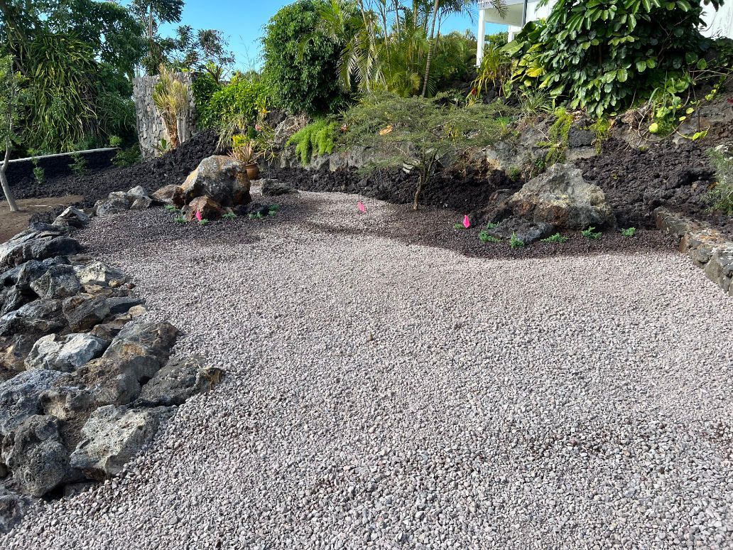 A gravel driveway surrounded by rocks and trees in a garden getting ready for Grading and landscaping. 