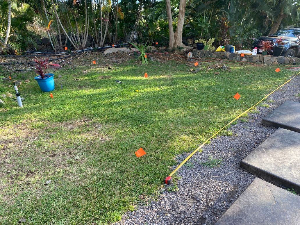 A yard with a yellow tape measure and orange markers on the grass getting ready for sprinkler system installation. 