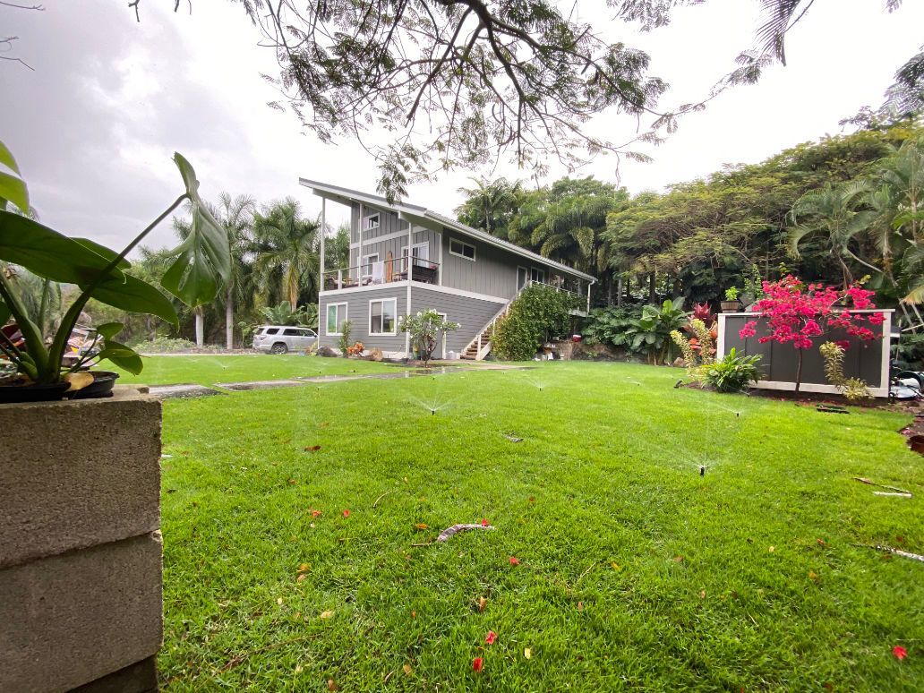A house is sitting in the middle of a lush green field with sprinkles on. 