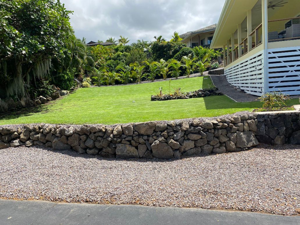 A house with a large lawn and a stone wall in front of it for a landscaping project. 