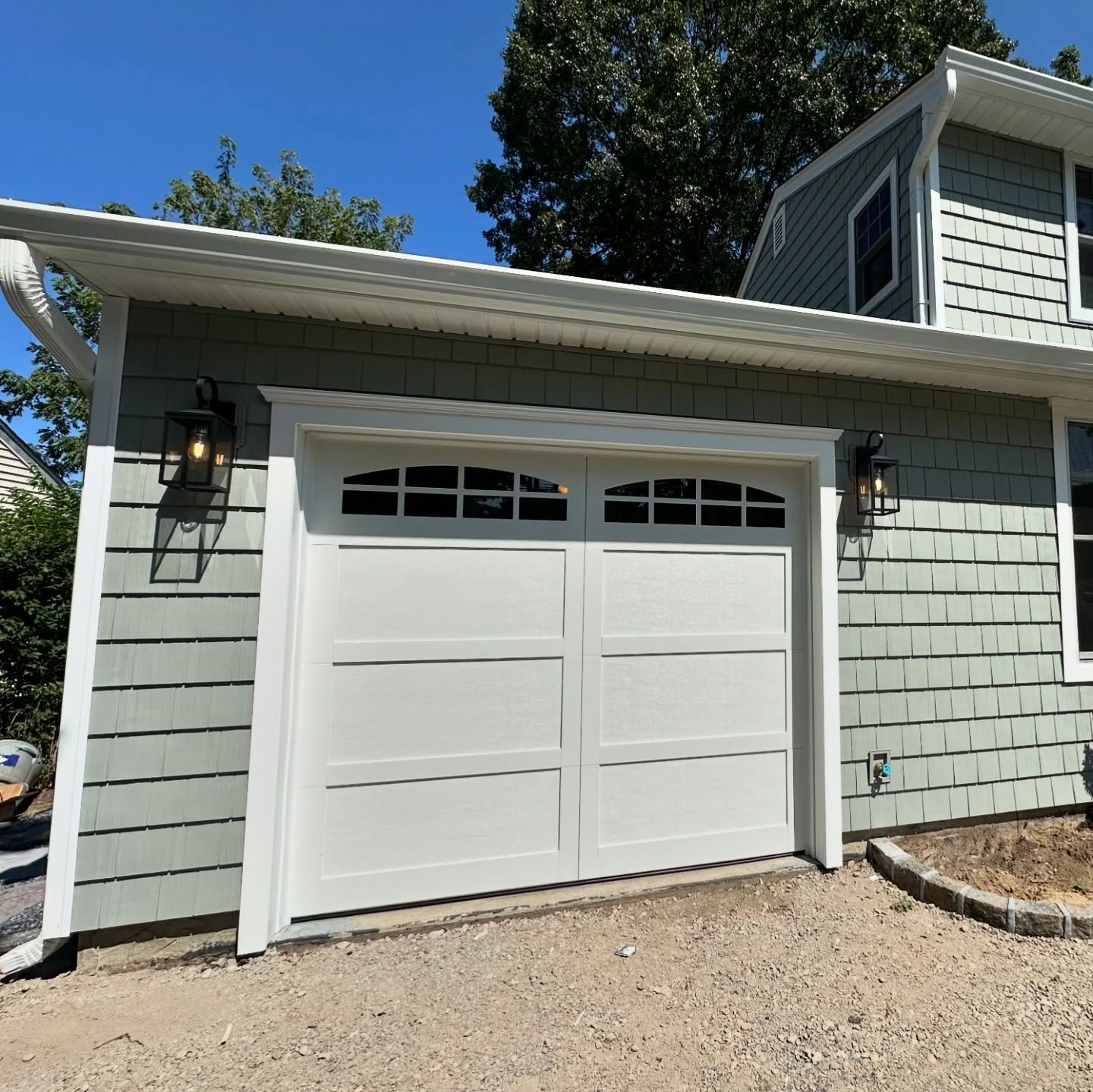Two black garage doors with horizontal window panels on a light gray siding house.