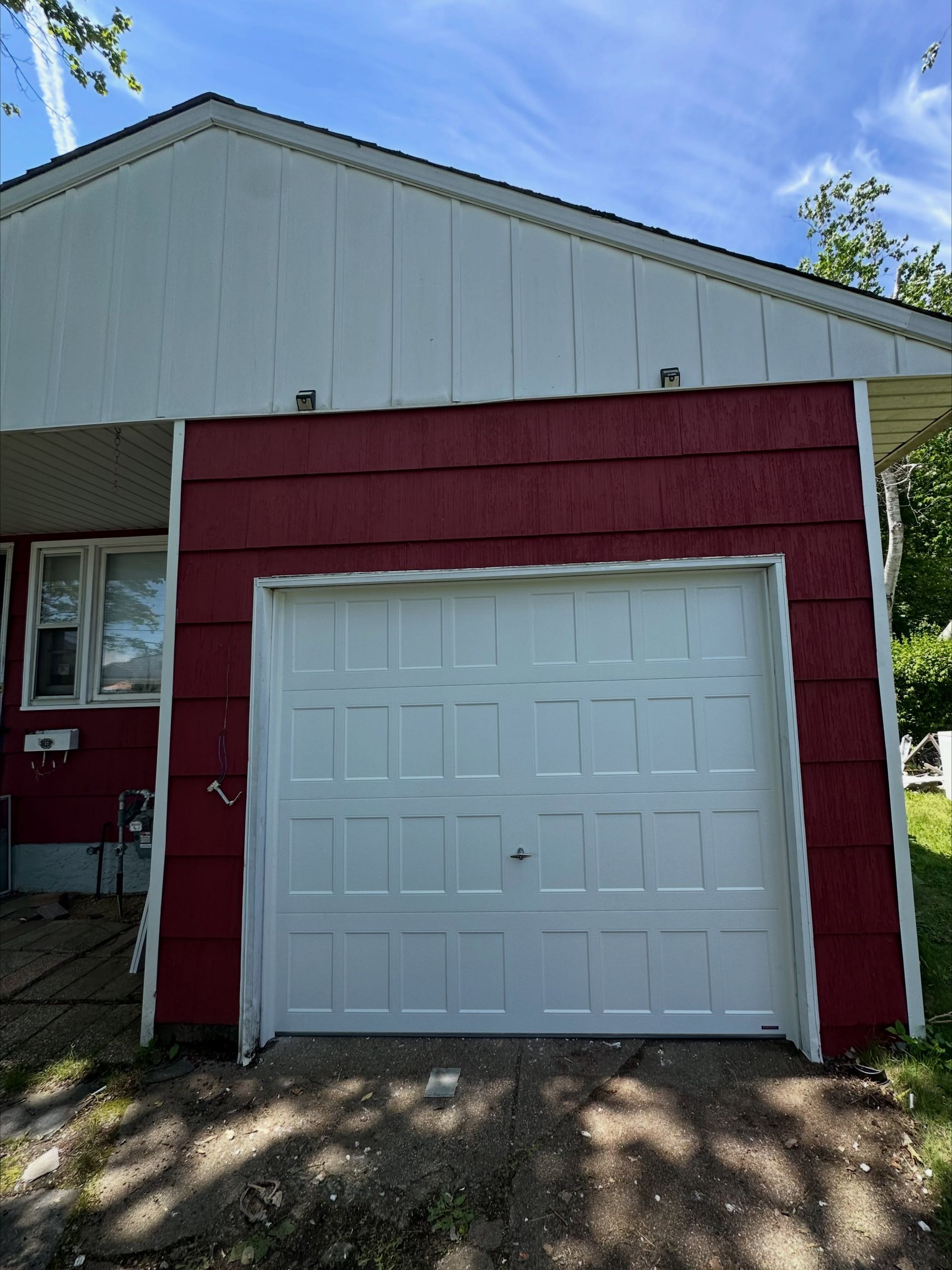 White garage door on a red and white house exterior with a small overhang.