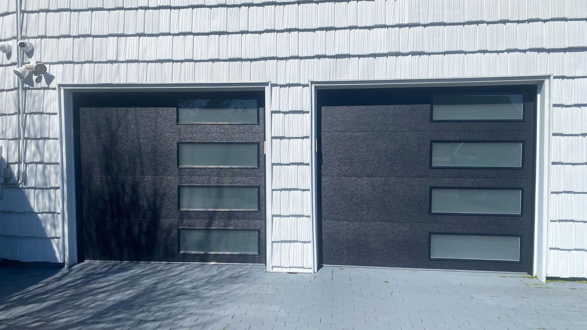 Two black garage doors with horizontal window panels on a light gray siding house.