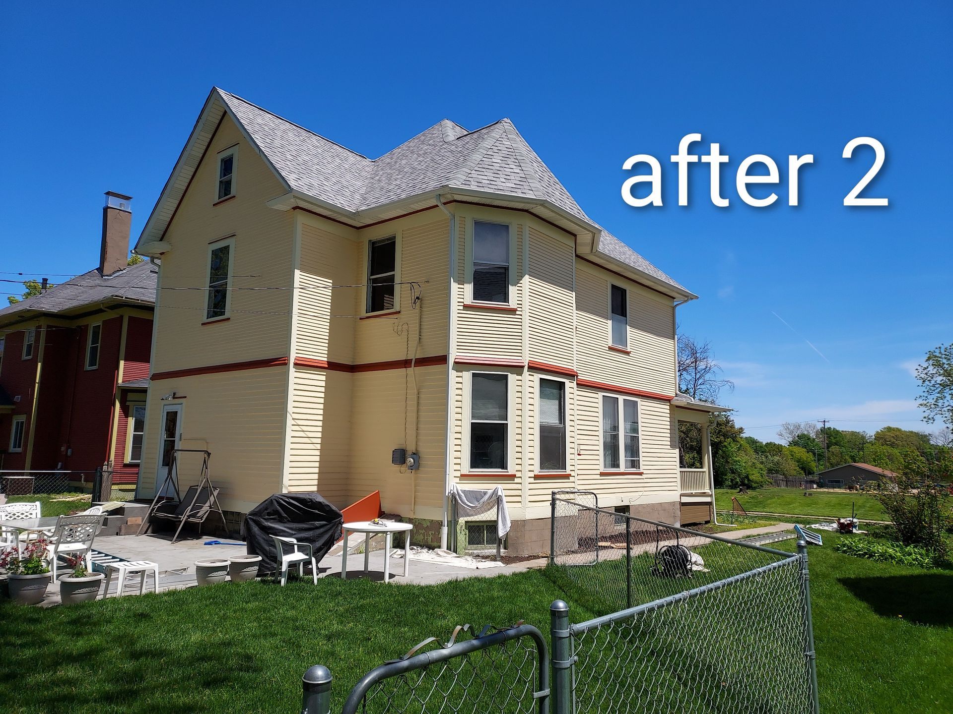 Renovated beige house with white trim and a gray roof, labeled “after 2,” beside a green yard and chain-link fence