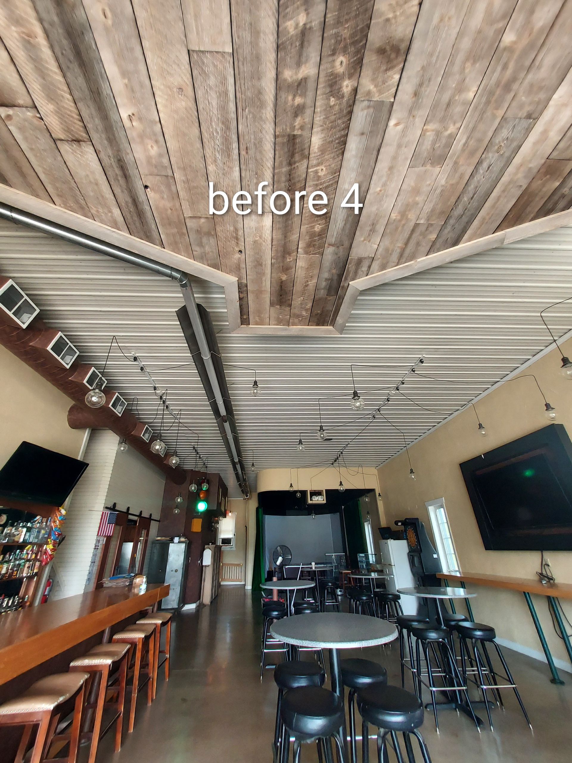 Rustic bar interior with wooden ceiling, stools along the counter, tables, and a wall-mounted TV