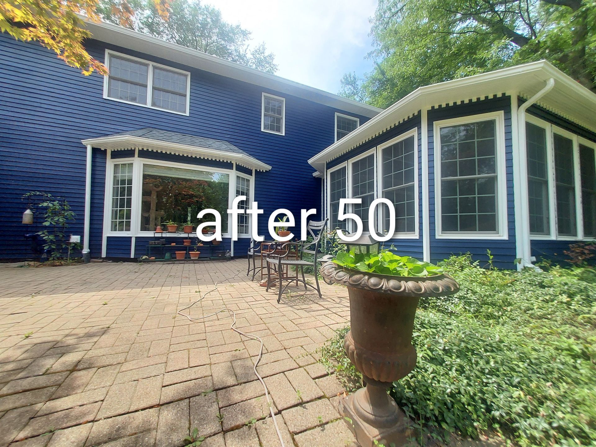 Blue house patio with white-trimmed windows, brick paving, and a potted plant; text reads “after 50”