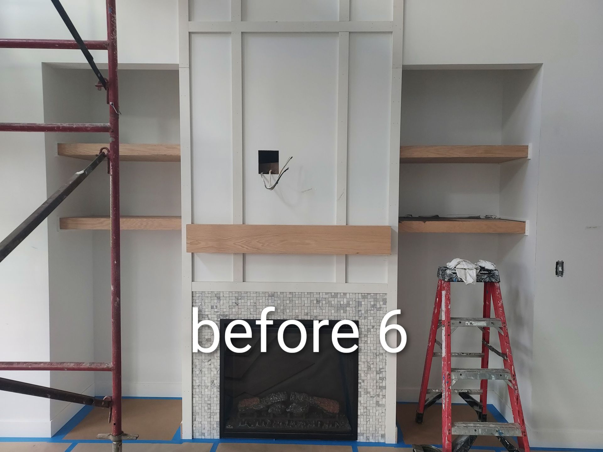 Living room fireplace wall with white built-ins, gray shelves, scaffold on left, and red ladder on right