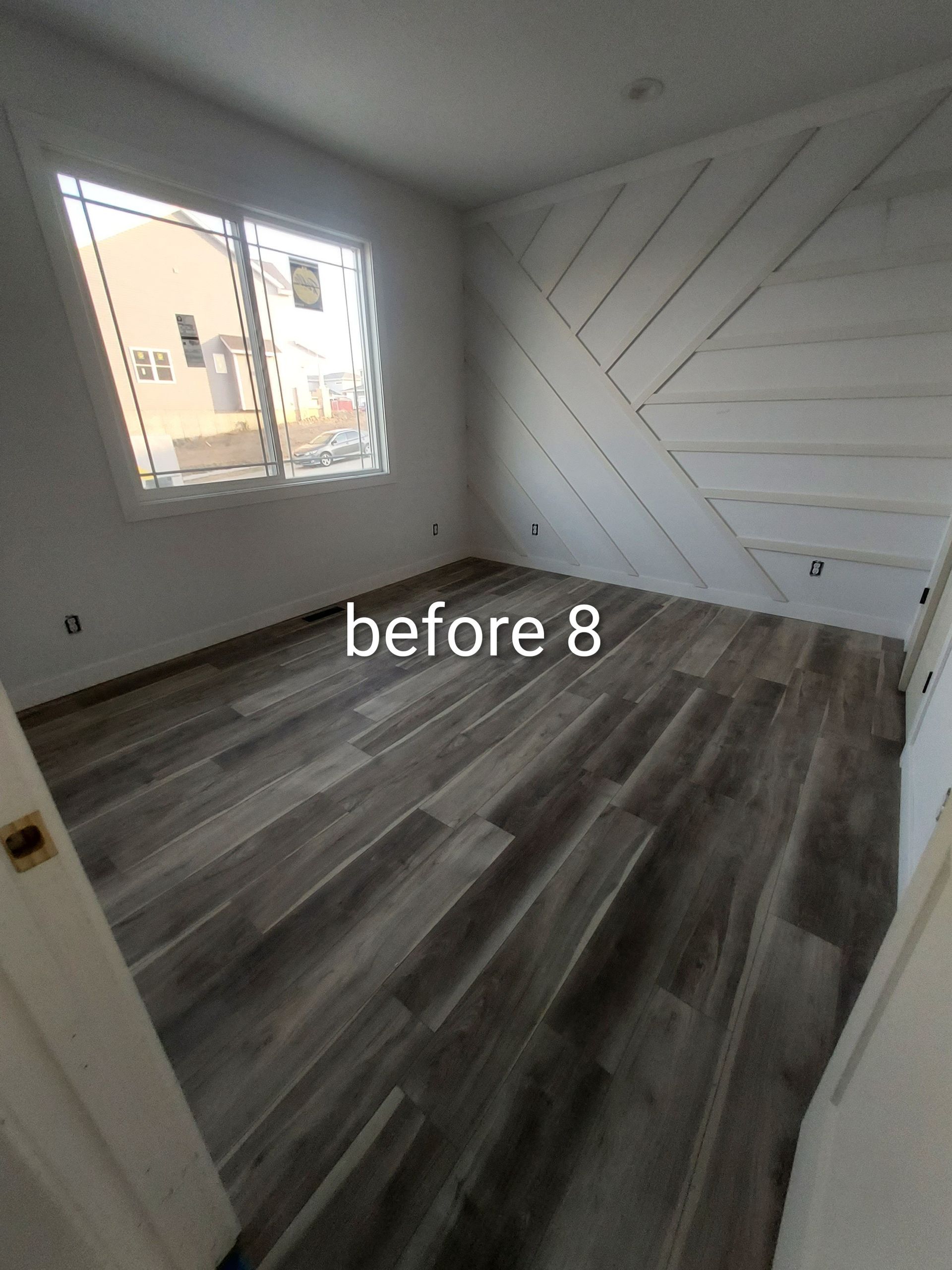 Empty room with gray wood-look flooring, white walls, and a window letting in daylight.