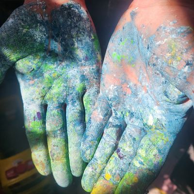 Open hands covered in colorful powder paint, palms facing up.