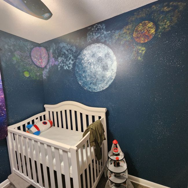 Space-themed nursery with crib, starry blue walls, and painted planets and moon