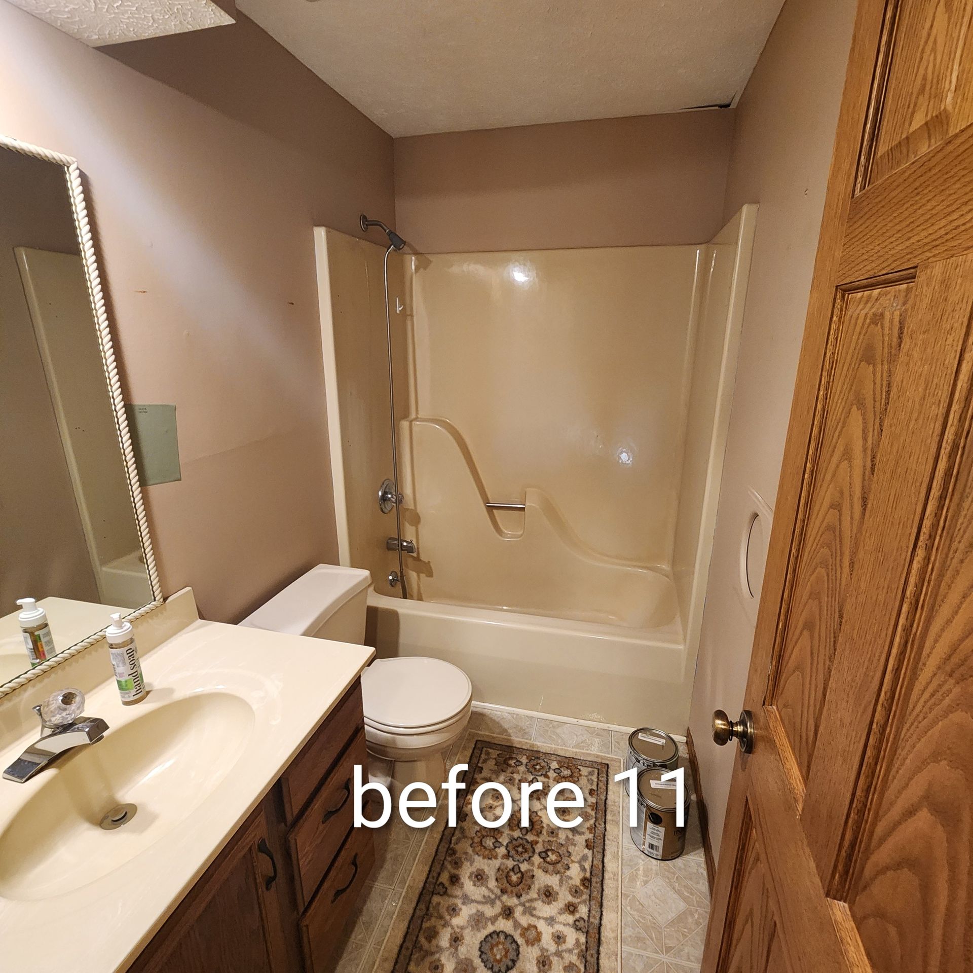 Bathroom with wood vanity, toilet, bathtub, and patterned rug; beige walls and shower curtain.