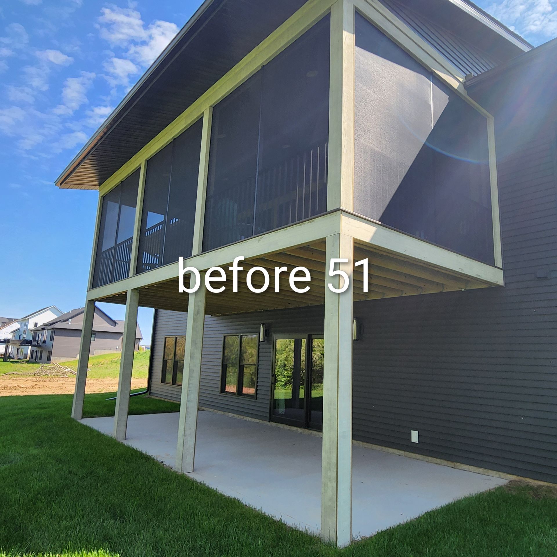 Back patio under an elevated deck beside a dark gray house on a sunny day