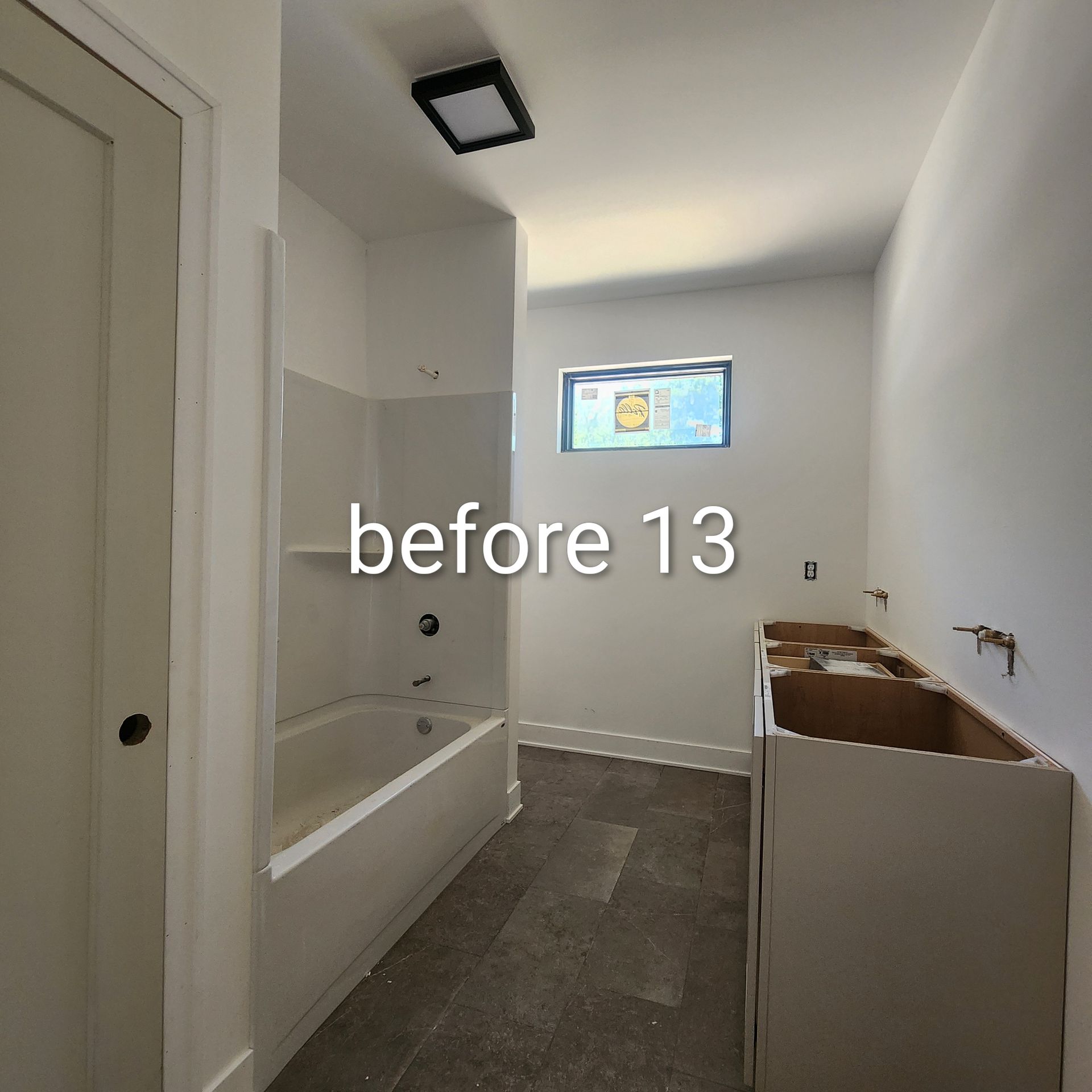 Small bathroom with white tub, gray floor, vanity, and a small window on the far wall.
