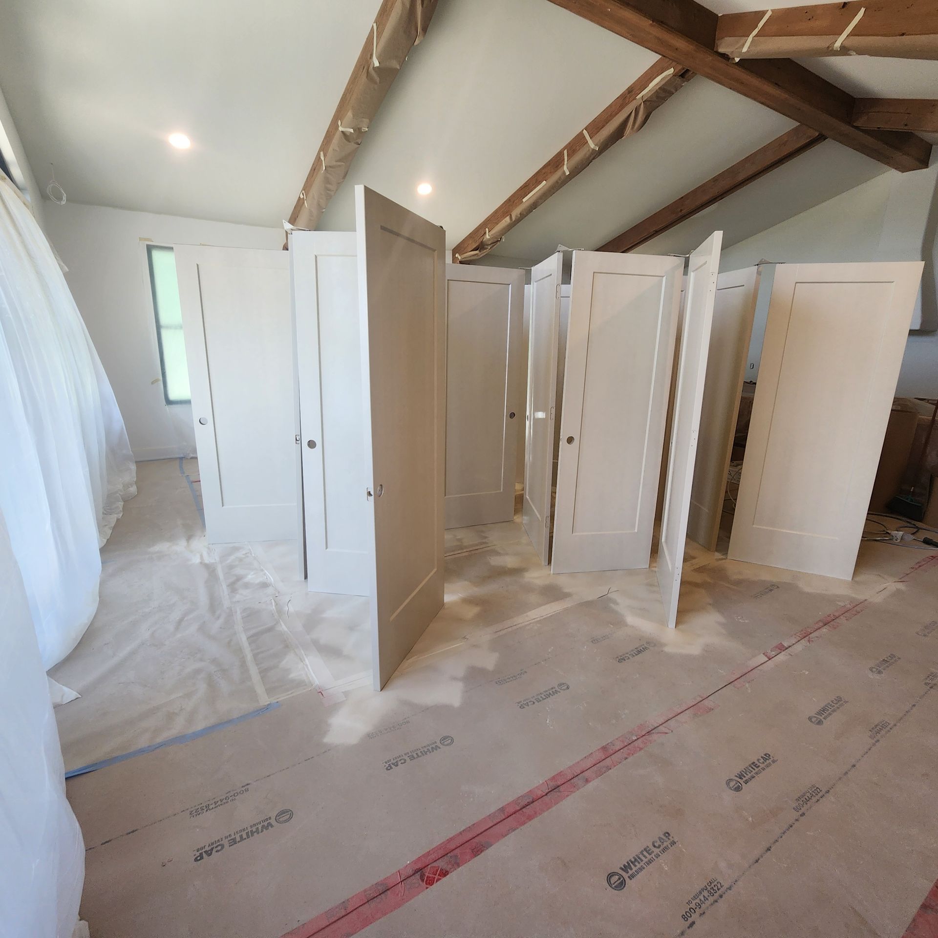 Partially painted room with multiple white doors standing open on a protective floor cover