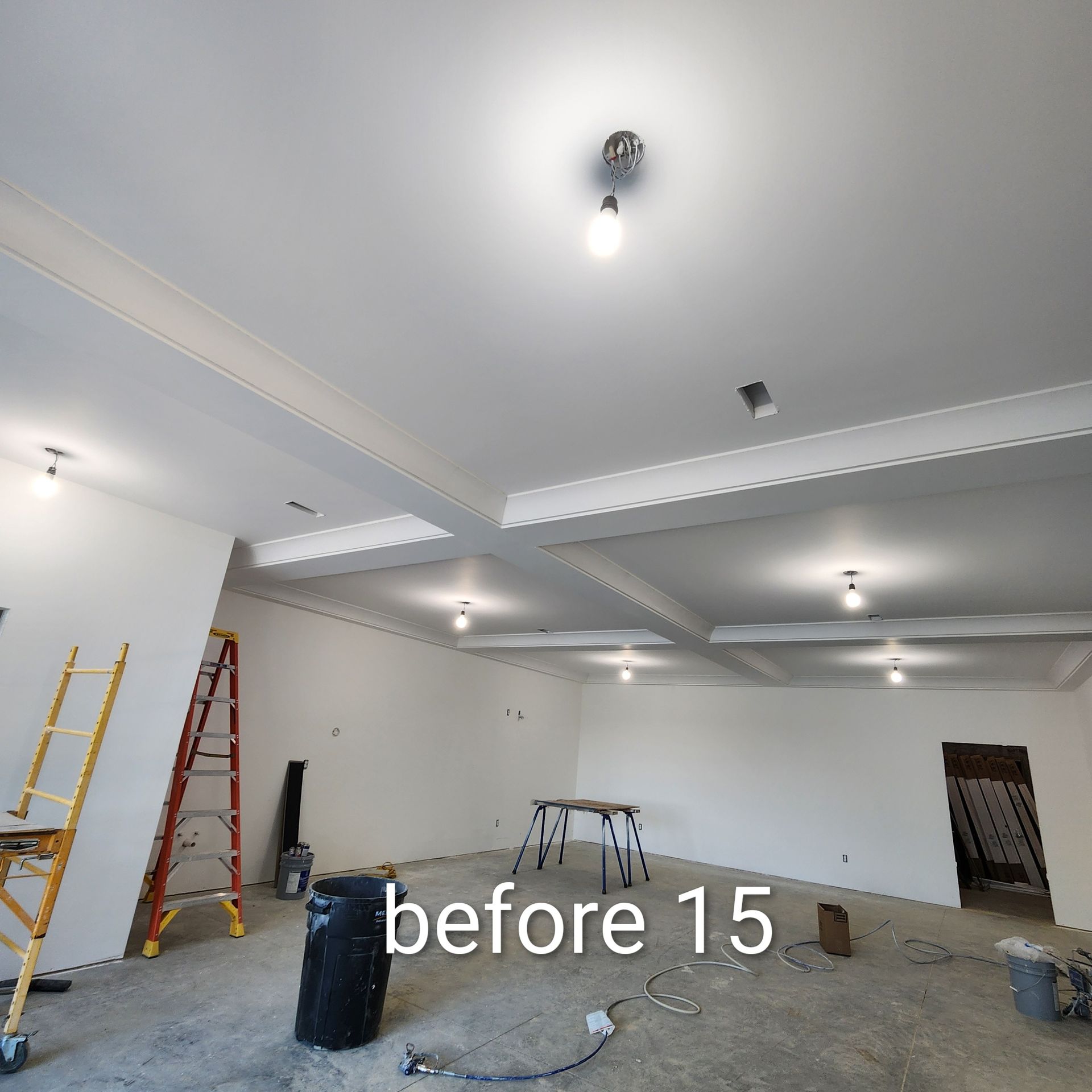 Unfinished room with white ceiling lights, ladders, and construction materials on the floor