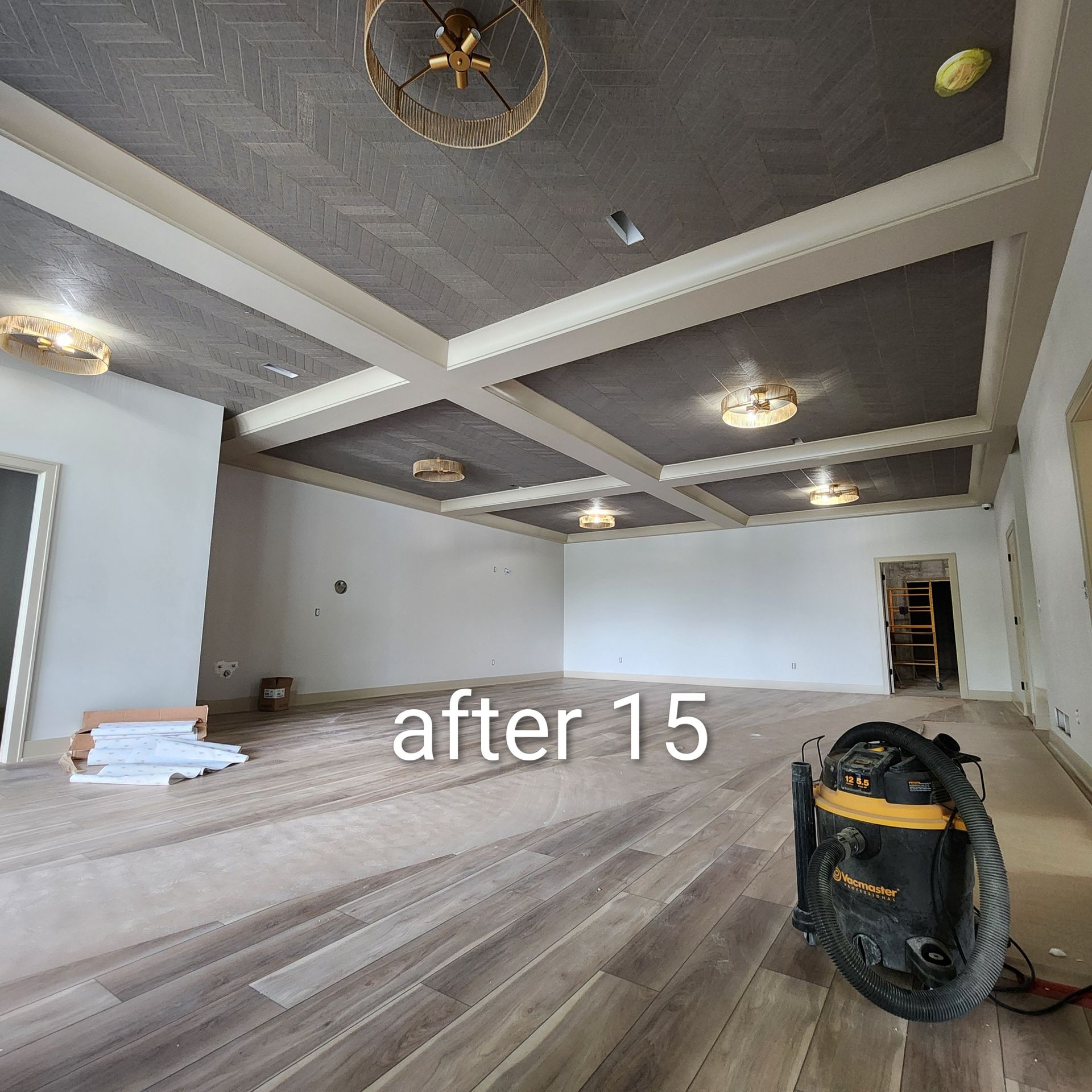 Spacious unfinished room with gray coffered ceiling, white walls, wood-look floor, and tools during renovation