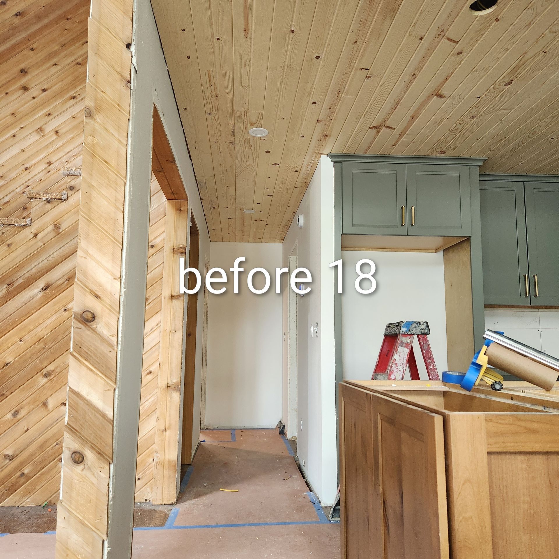 Half-finished hallway and kitchen with wood ceiling, white walls, and cabinets under renovation