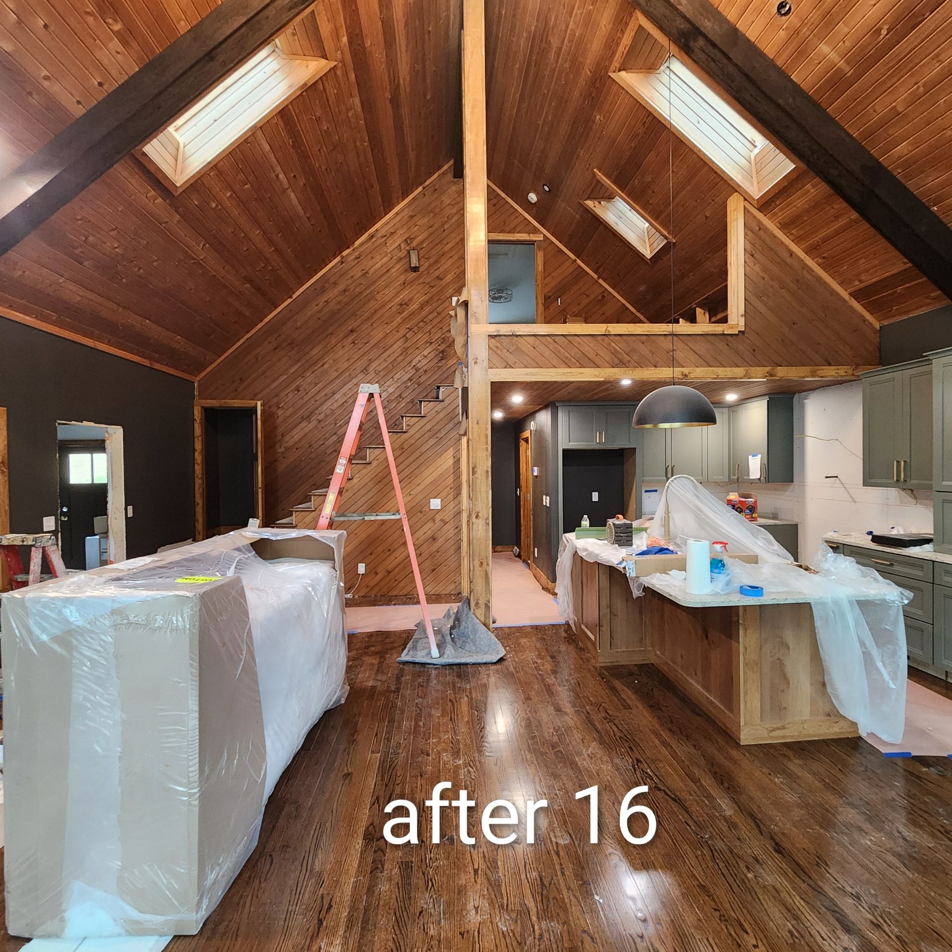 Unfinished loft interior with wood ceiling, skylights, plastic-covered cabinets, and a ladder on the floor