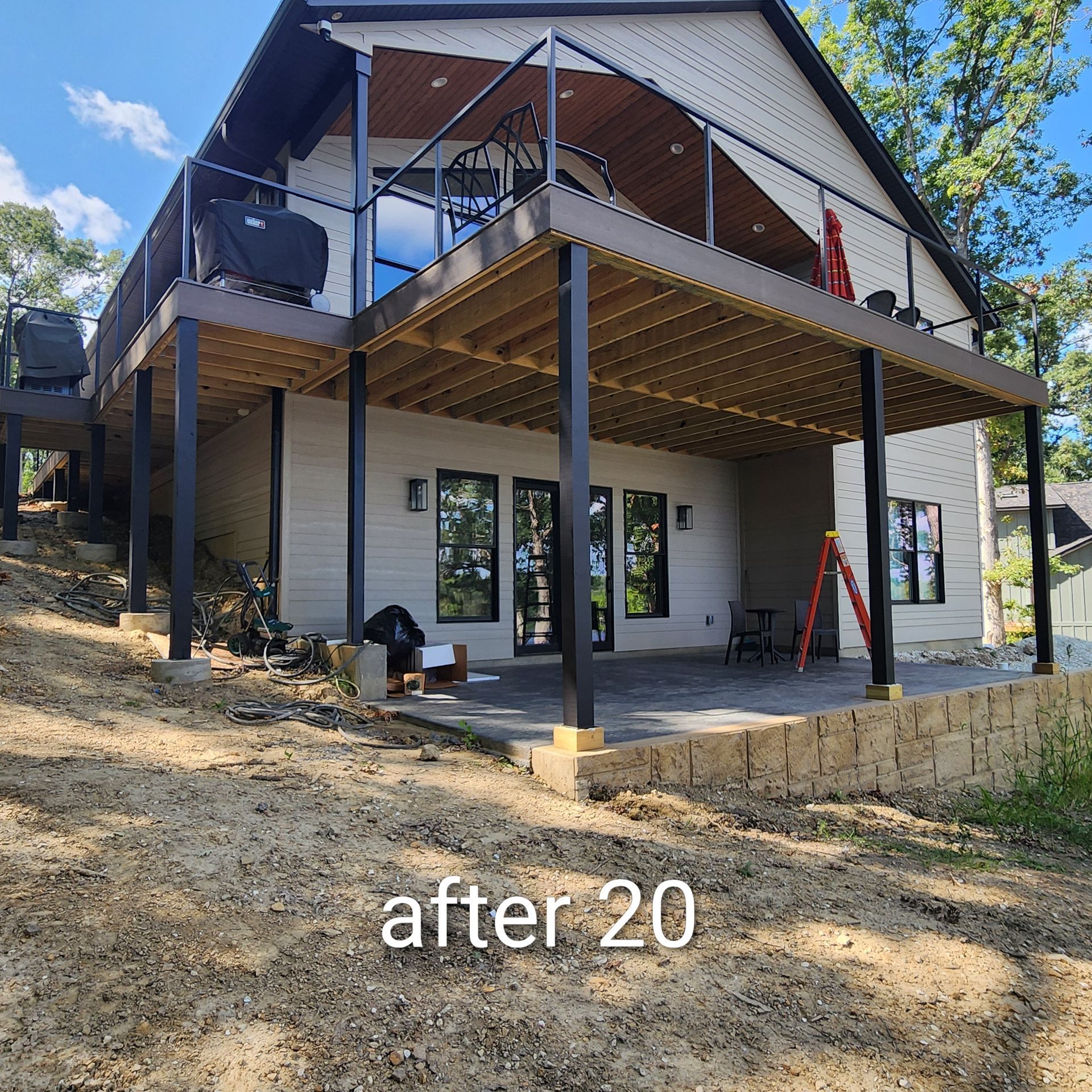 Modern house exterior with upper deck, black posts, and text “after 20” over a sloped dirt yard