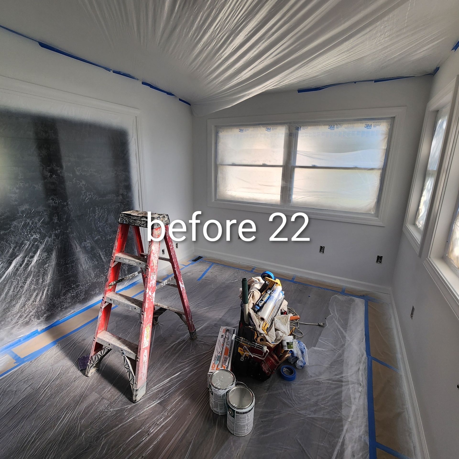 Painted room under renovation with red ladder, tools, and plastic-covered floor and windows.