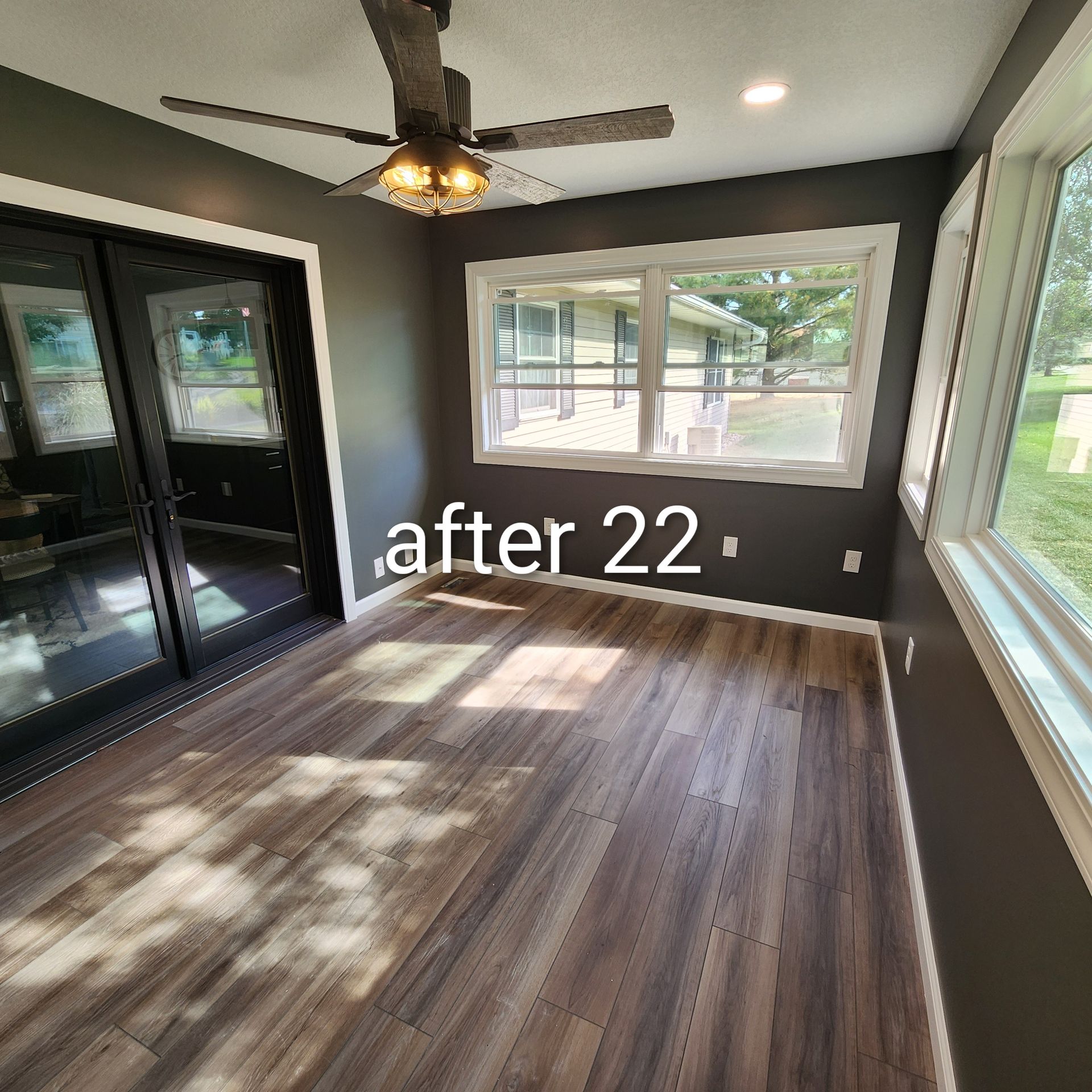 Sunroom with dark walls, wood-look floor, ceiling fan, and large windows; text reads “after 22.”