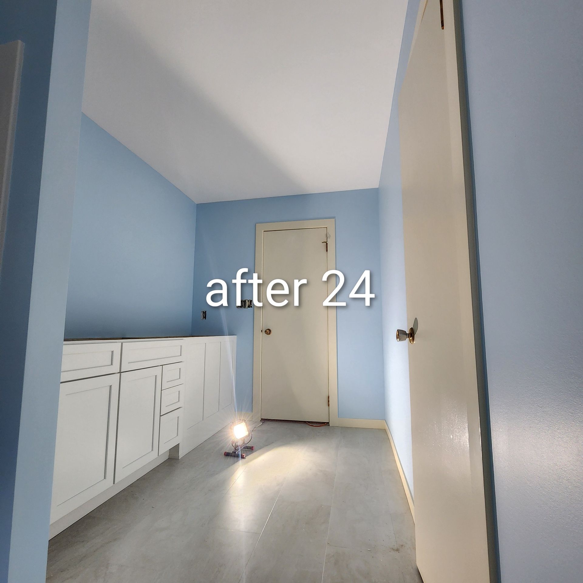 Small blue kitchen after 24 hours, with white cabinets, a closed door, and a floor light drying the room.