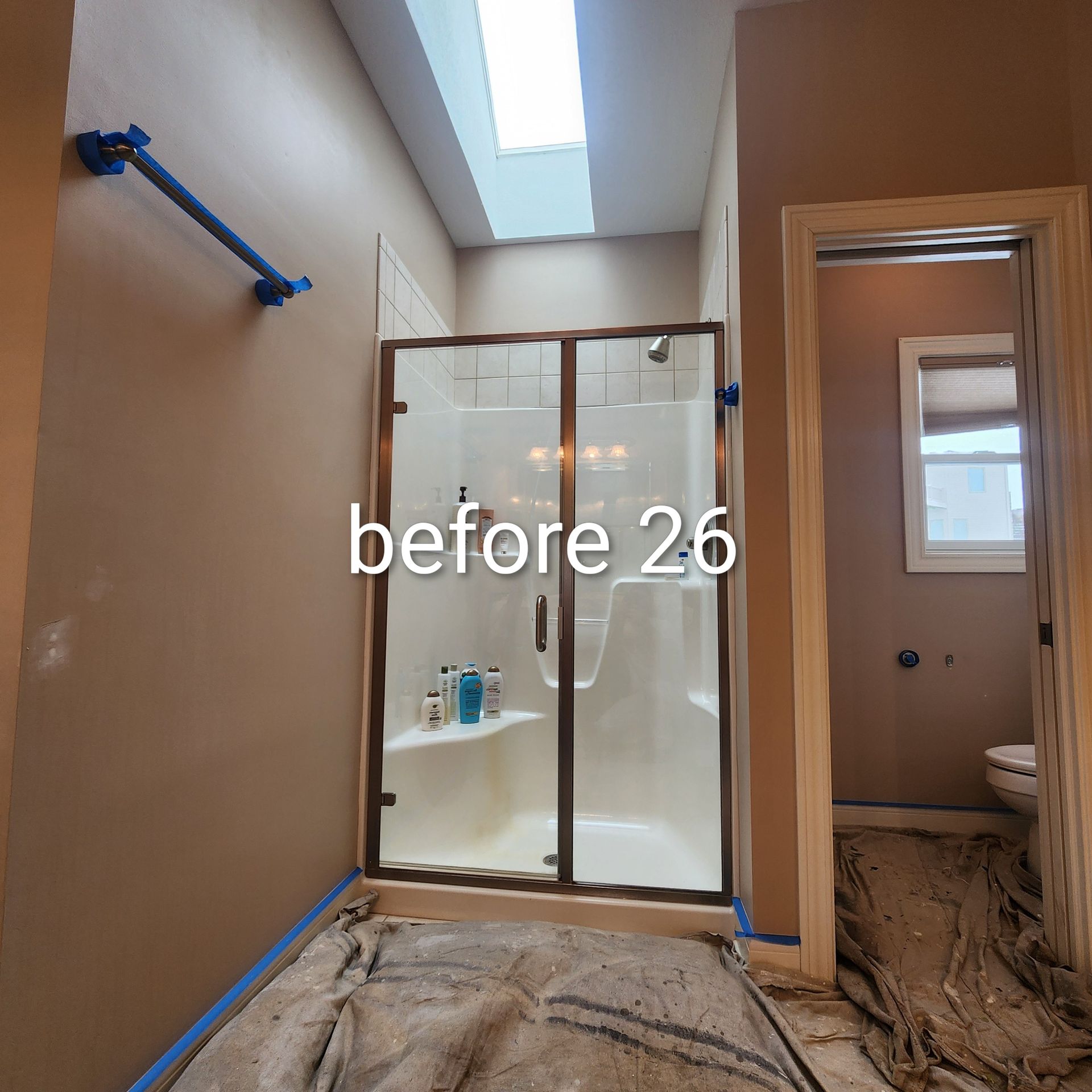 Bathroom under renovation with shower enclosure, tan walls, skylight, and plastic-covered floor.