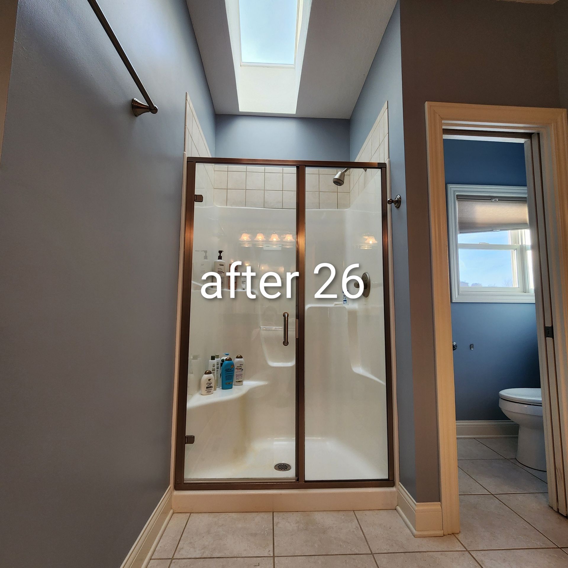 Small bathroom with a glass shower, skylight, and open doorway to a toilet room; “after 26” text over shower.