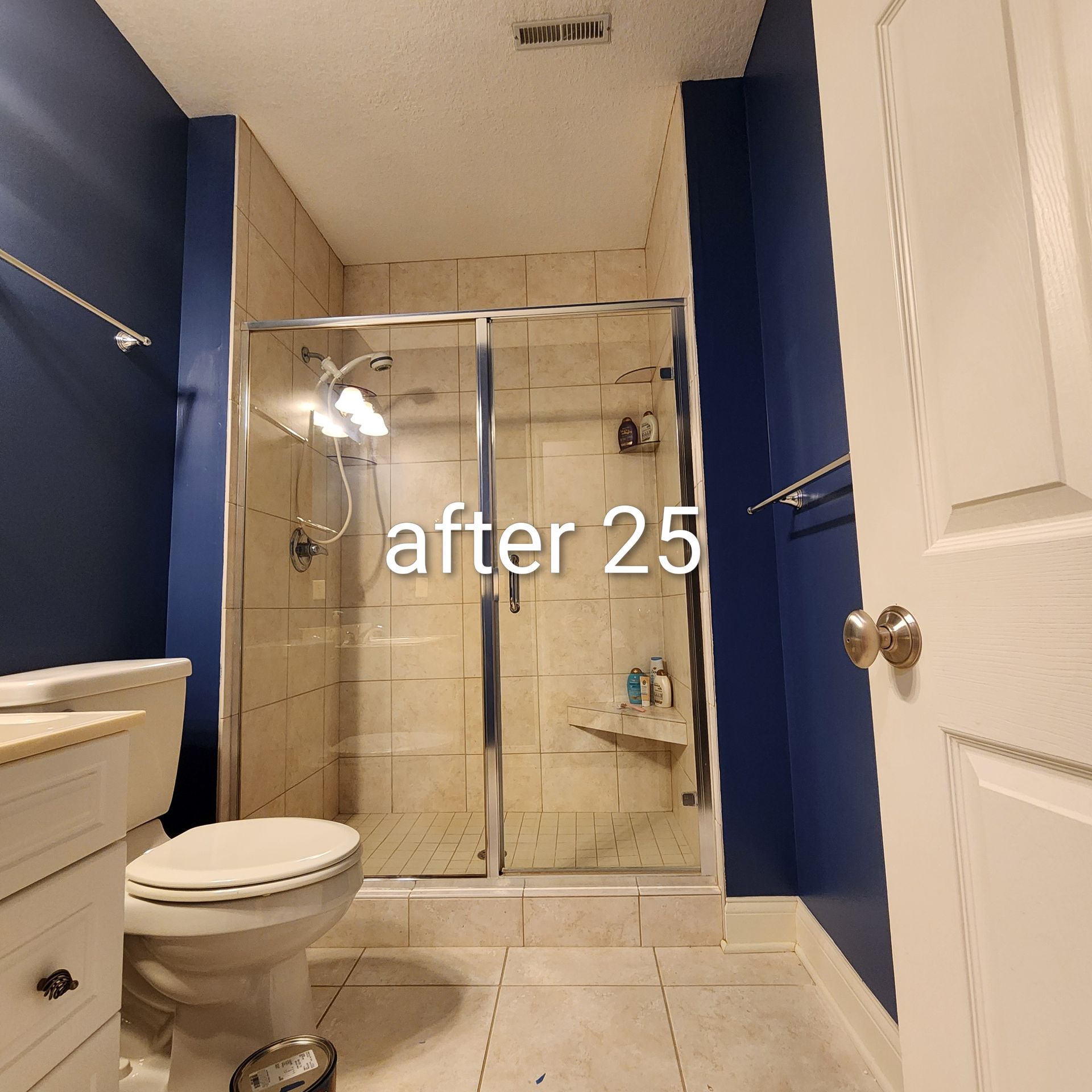 Small bathroom with beige tile, blue walls, white sink and toilet, and a glass shower labeled “after 25.”