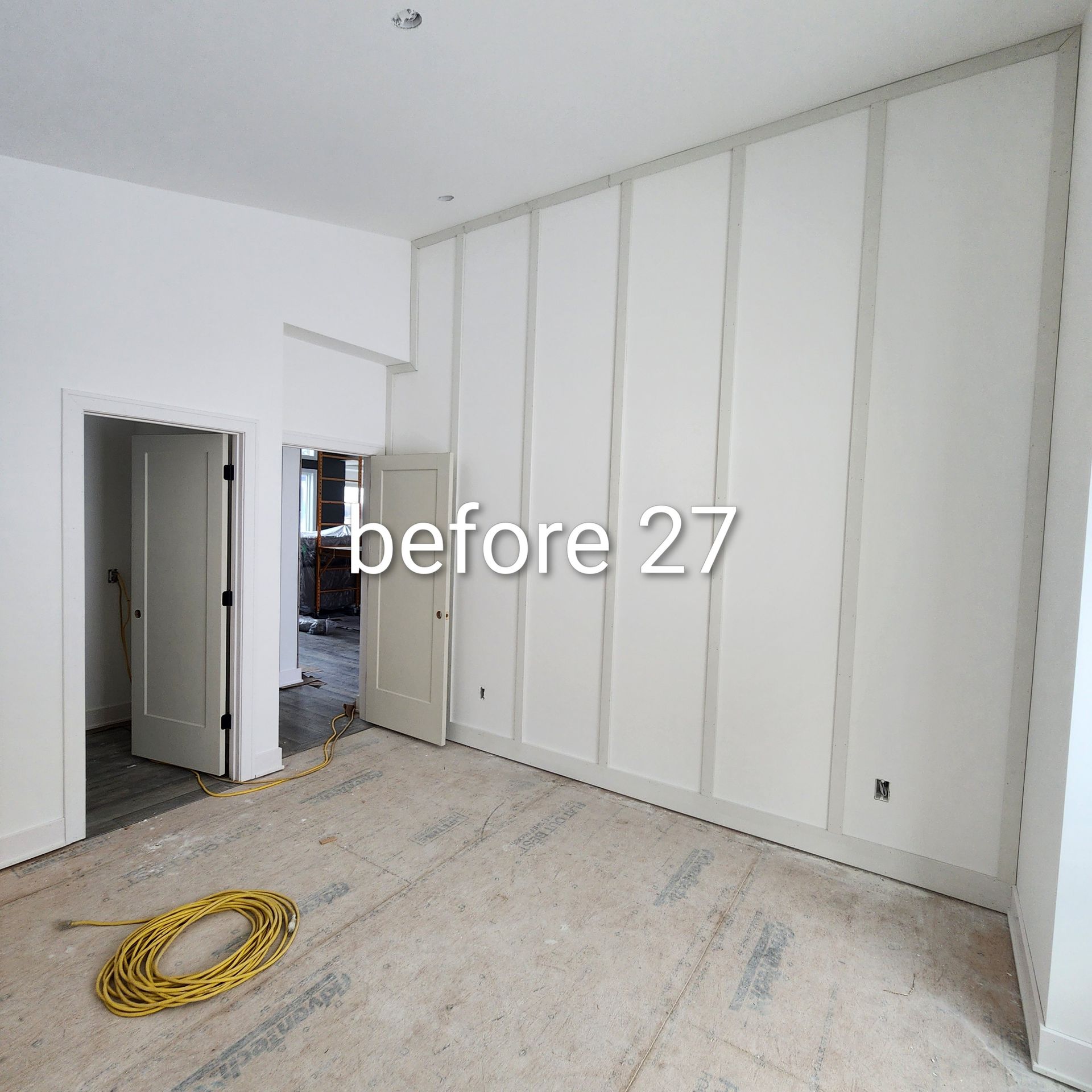 Empty white room under renovation with unfinished walls, exposed doorway, and a yellow coiled hose on the floor