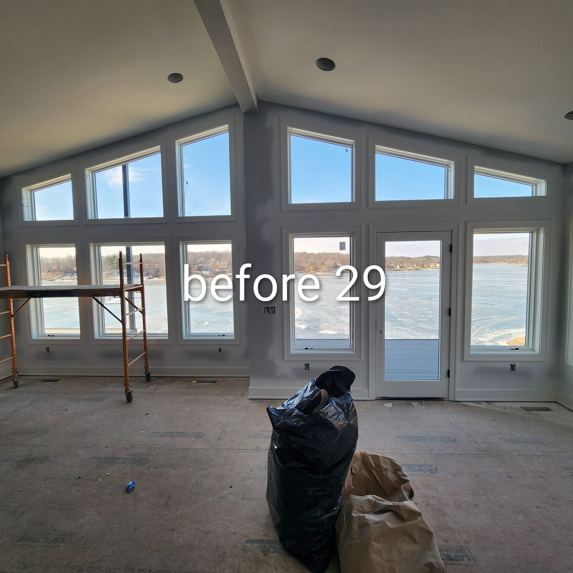 Spacious unfinished room with large windows and glass doors overlooking water, with construction materials on the floor.