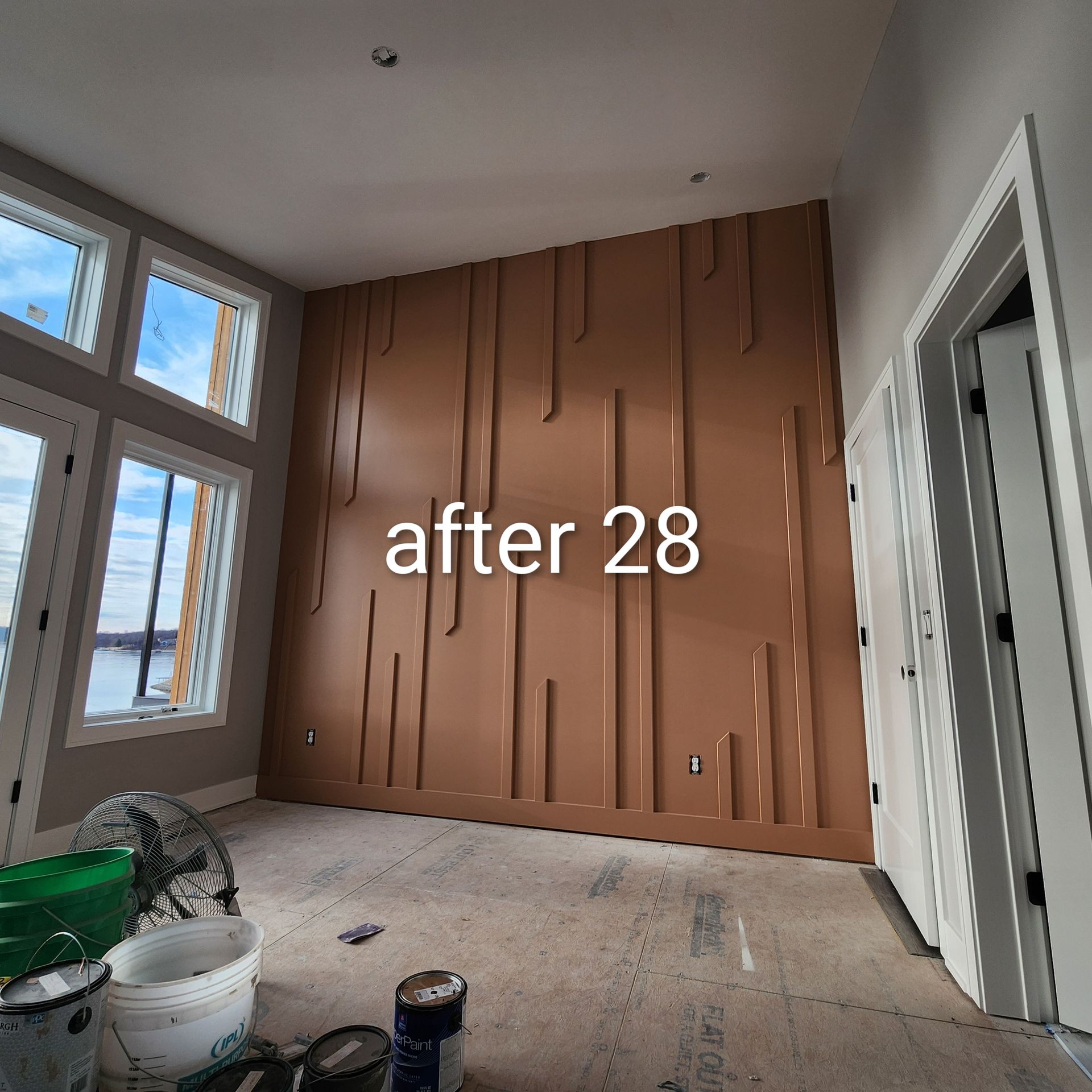 Partially finished room with brown paneled accent wall, windows, and construction materials on the floor.