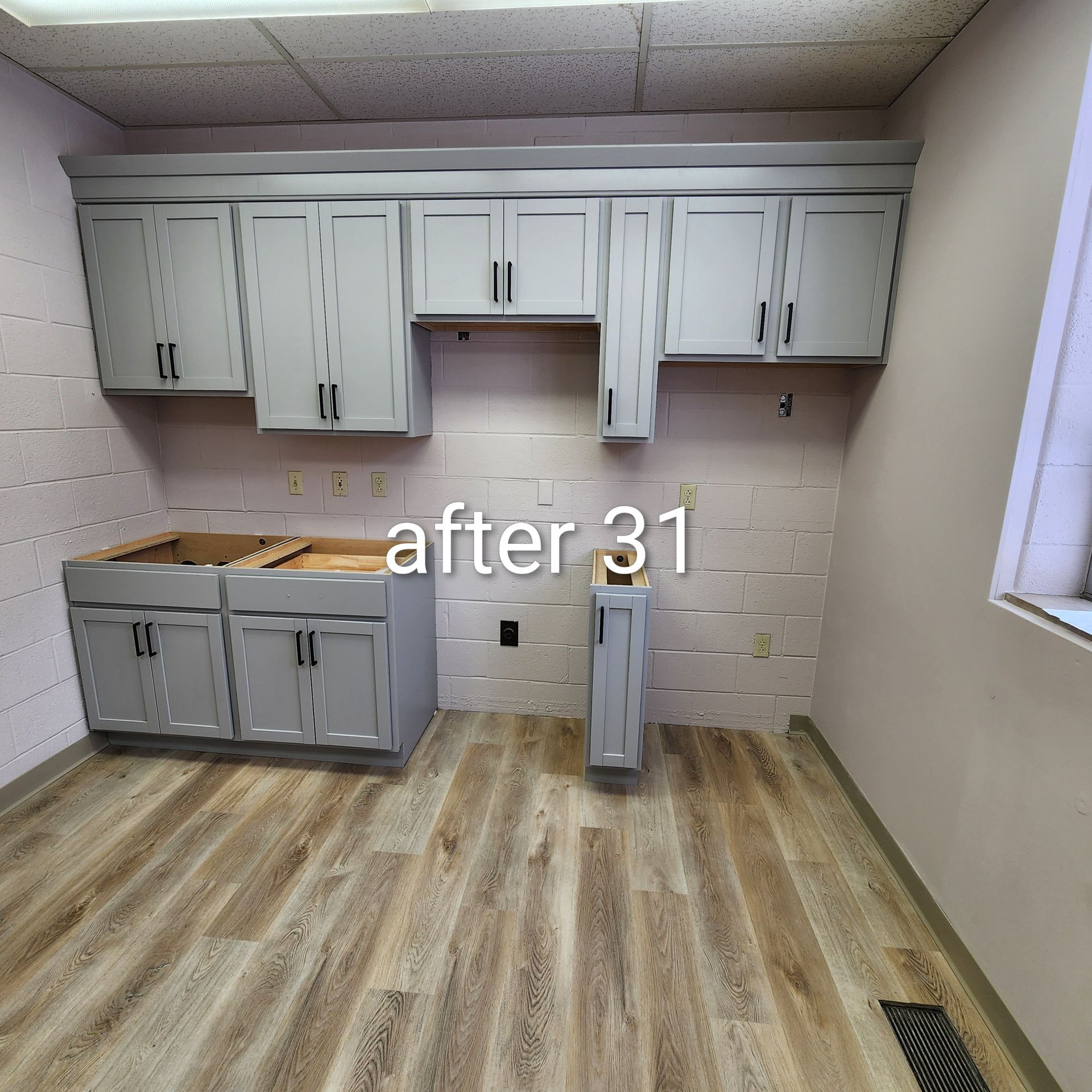 Renovated small kitchen with white cabinets, gray backsplash, wood-look floor, and a window on the right