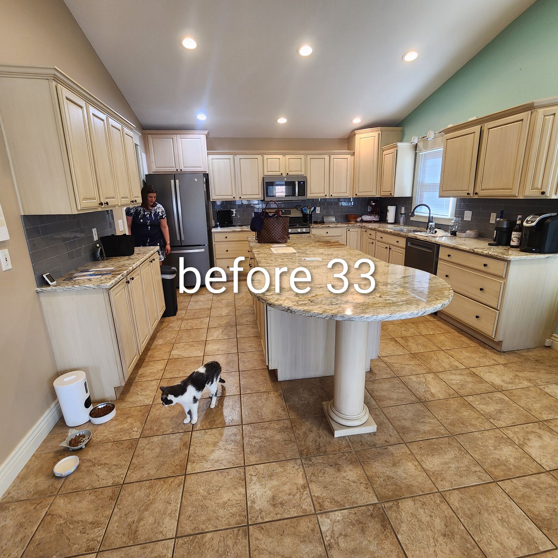Bright kitchen with cream cabinets, tiled floor, island table, and a small black-and-white dog near the center.