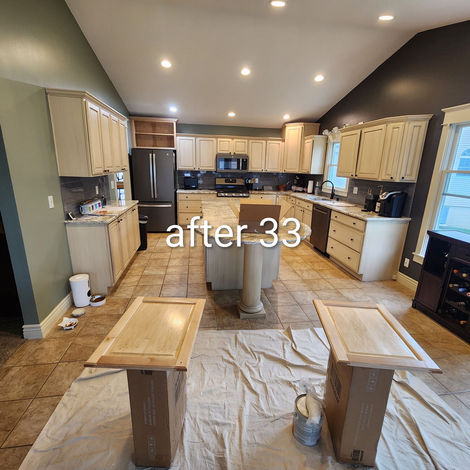 Kitchen under renovation with taped cabinets, floor protection, and two work tables in the foreground.