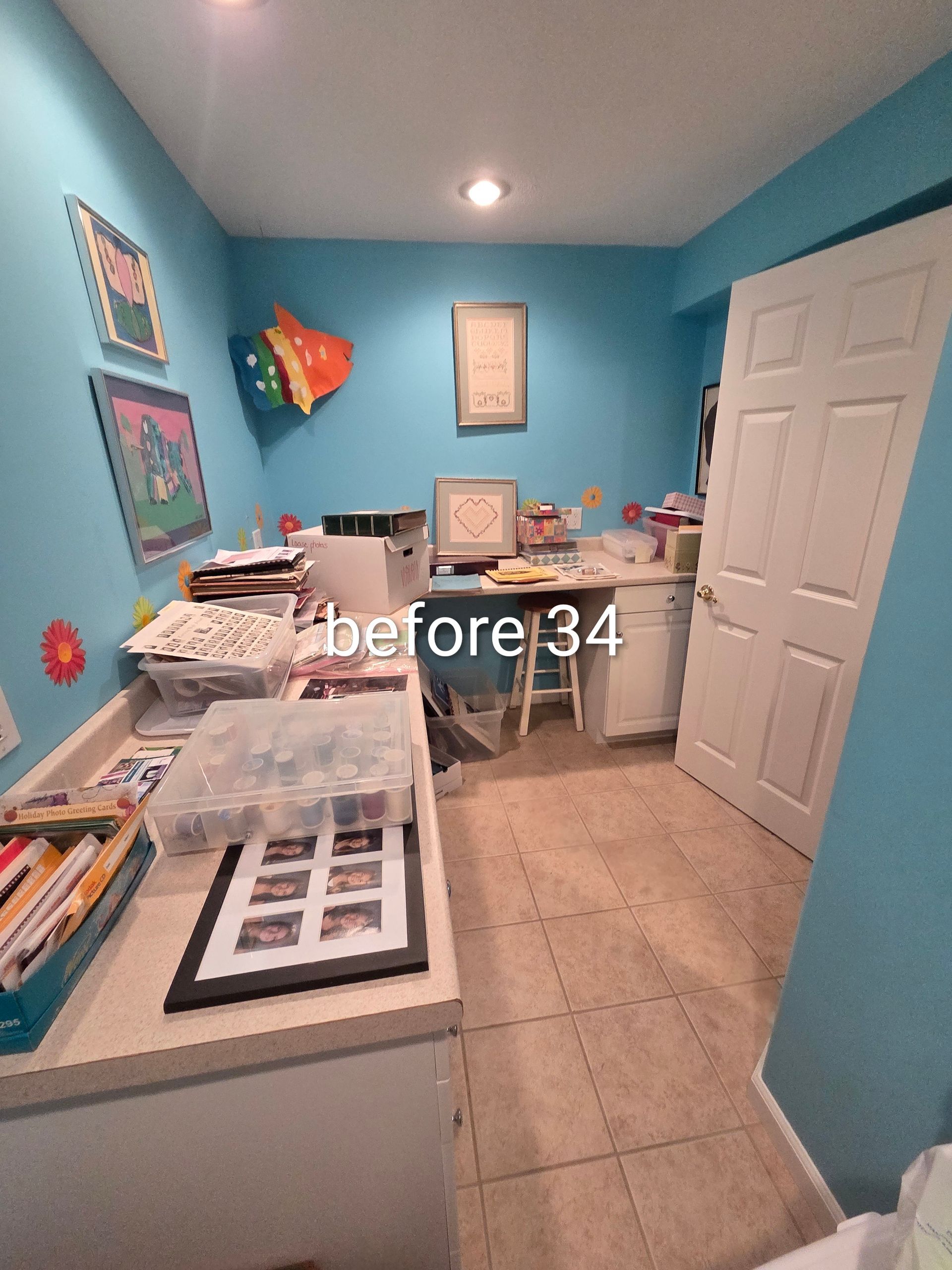 Blue home office with desks, papers, printer, and a white closet door on tan tile floor.