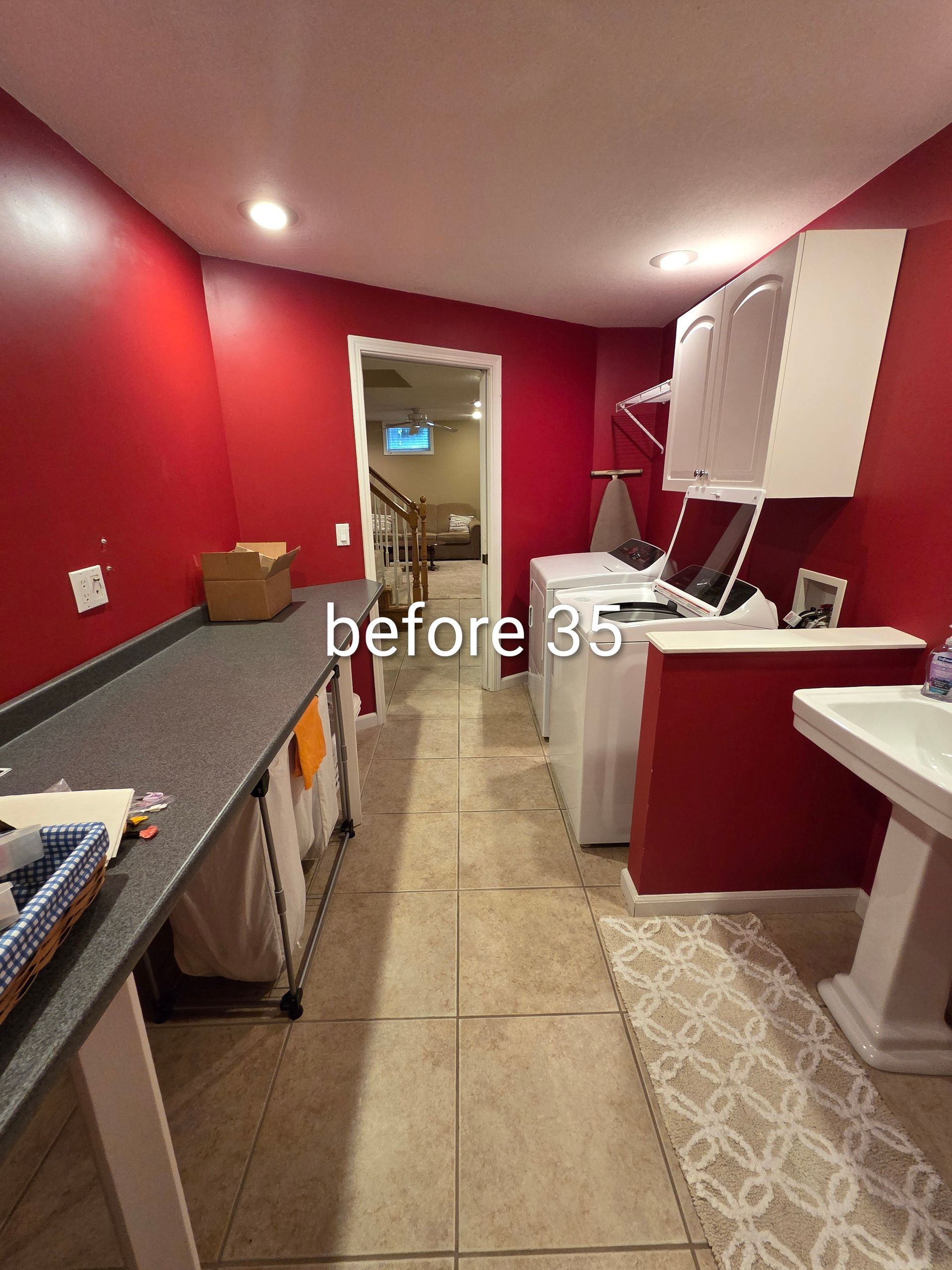 Narrow laundry room with red walls, sink, washer, and drying rack, viewed from the doorway