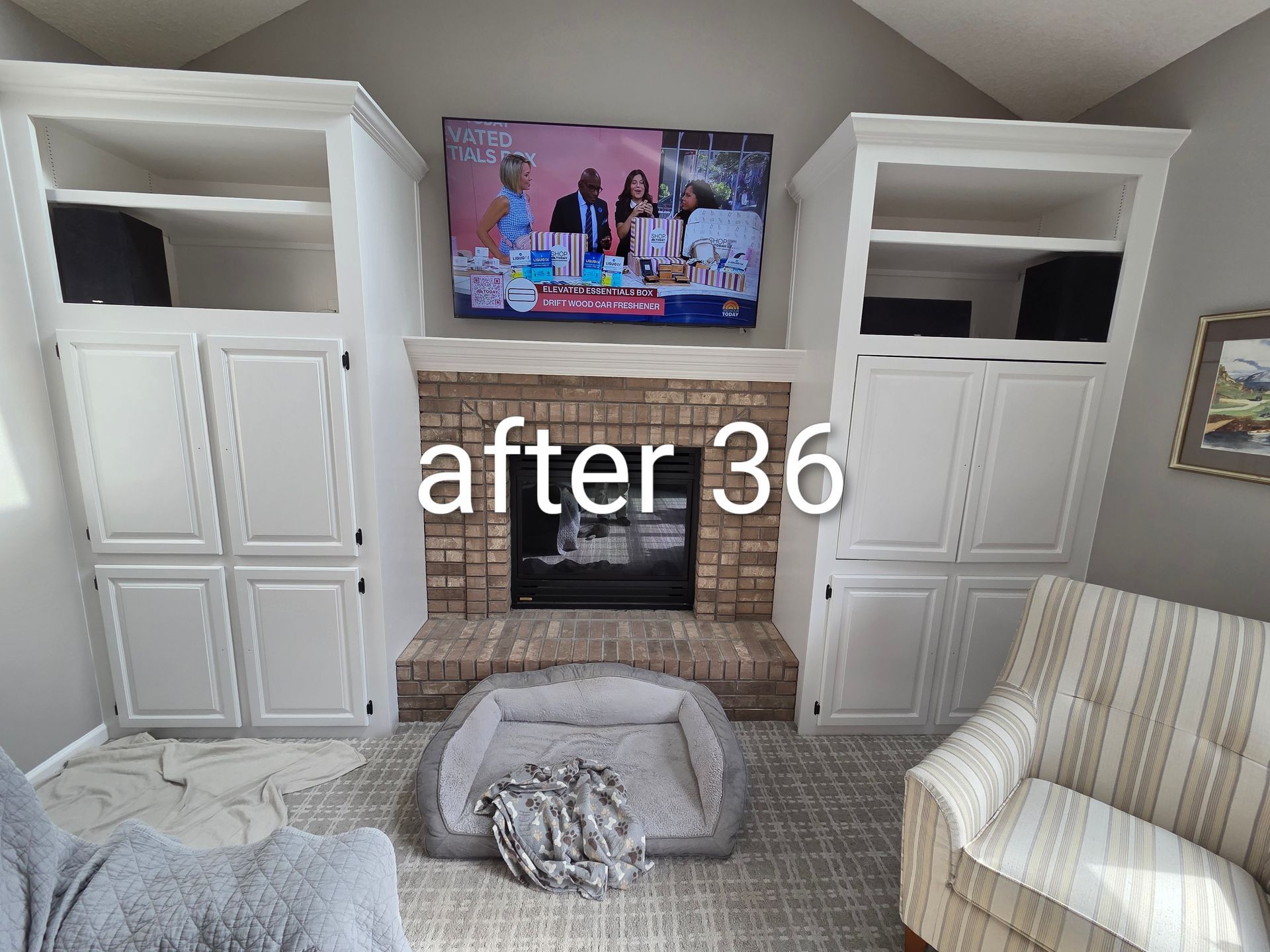 Living room with built-in white shelves, brick fireplace, TV, and a gray dog bed on the floor