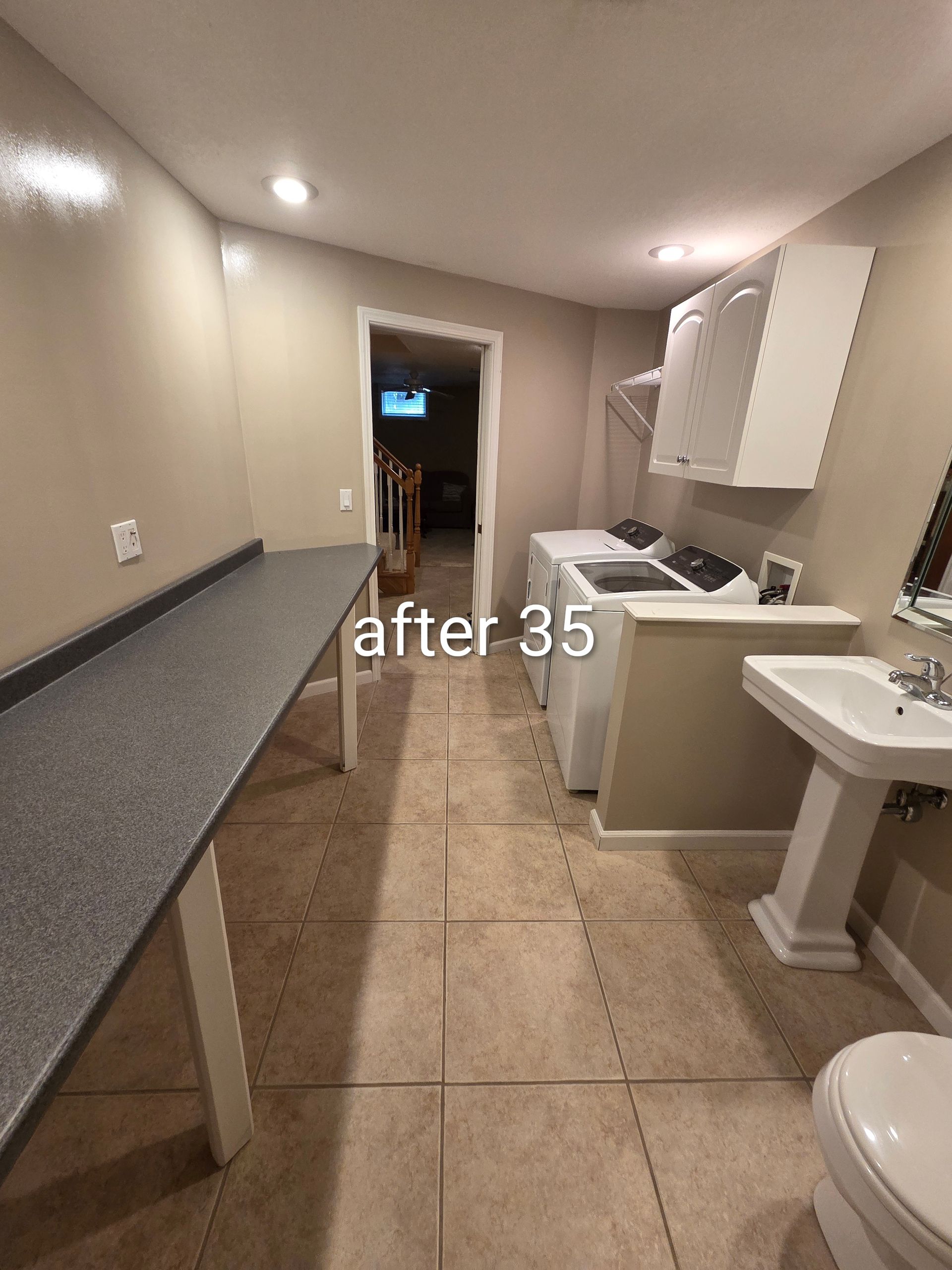 Narrow motel room with two beds, a sink, and gray countertops under beige walls and warm lighting