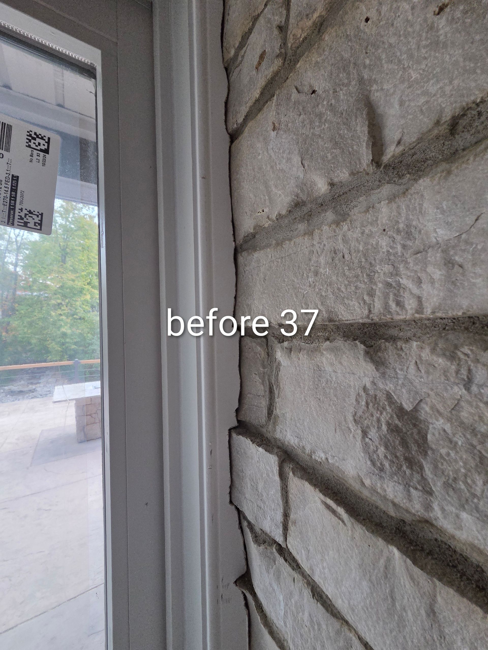 Close-up of a stone wall beside a window and doorway, with outdoor pavement and trees visible outside.