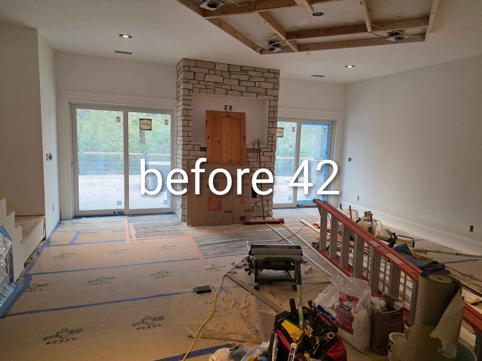 Living room under renovation with exposed ceiling, fireplace, sliding door, and tools on the floor
