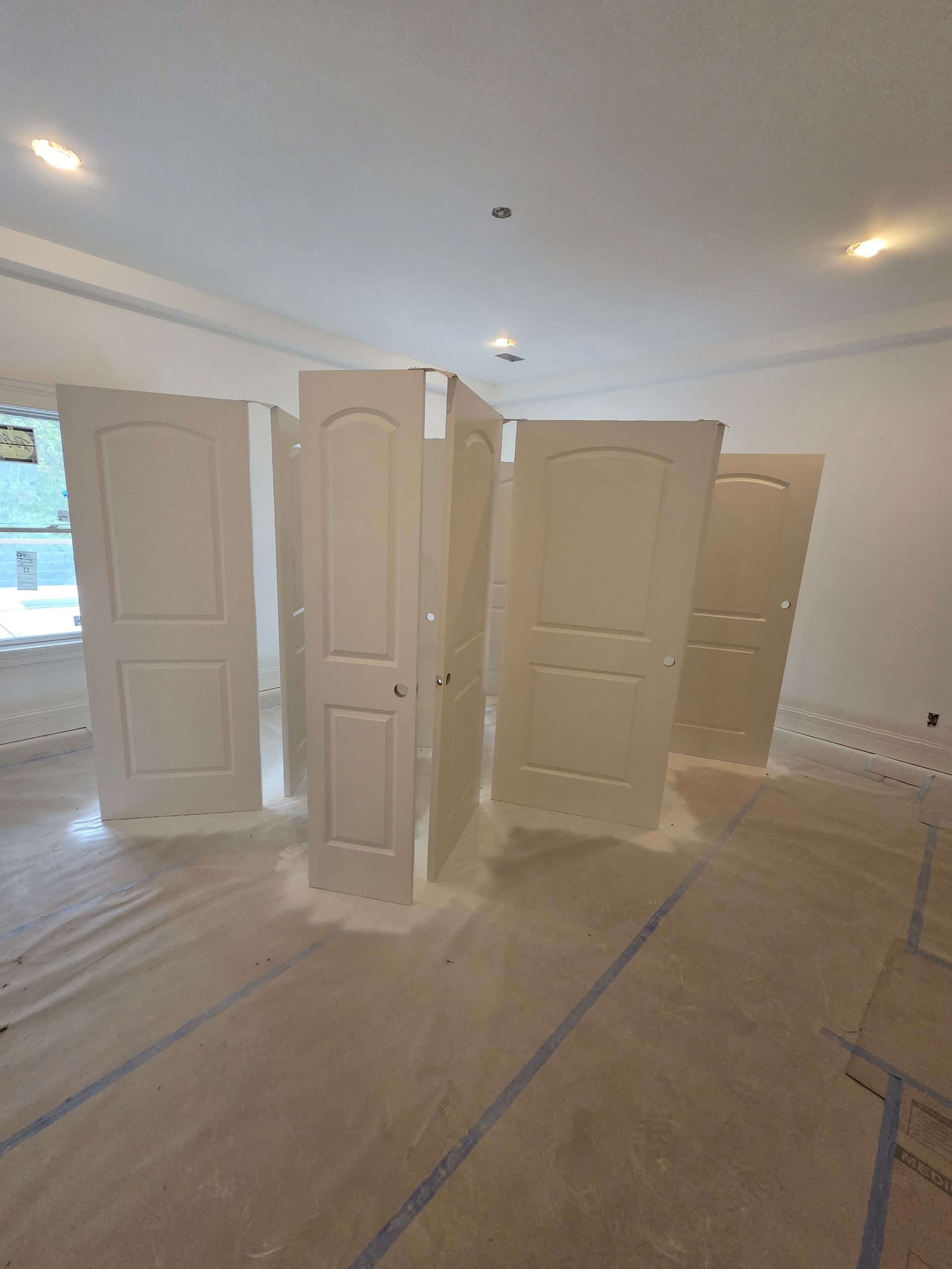 White interior with several doors arranged in a room, floor protected by taped-down covering during renovation.