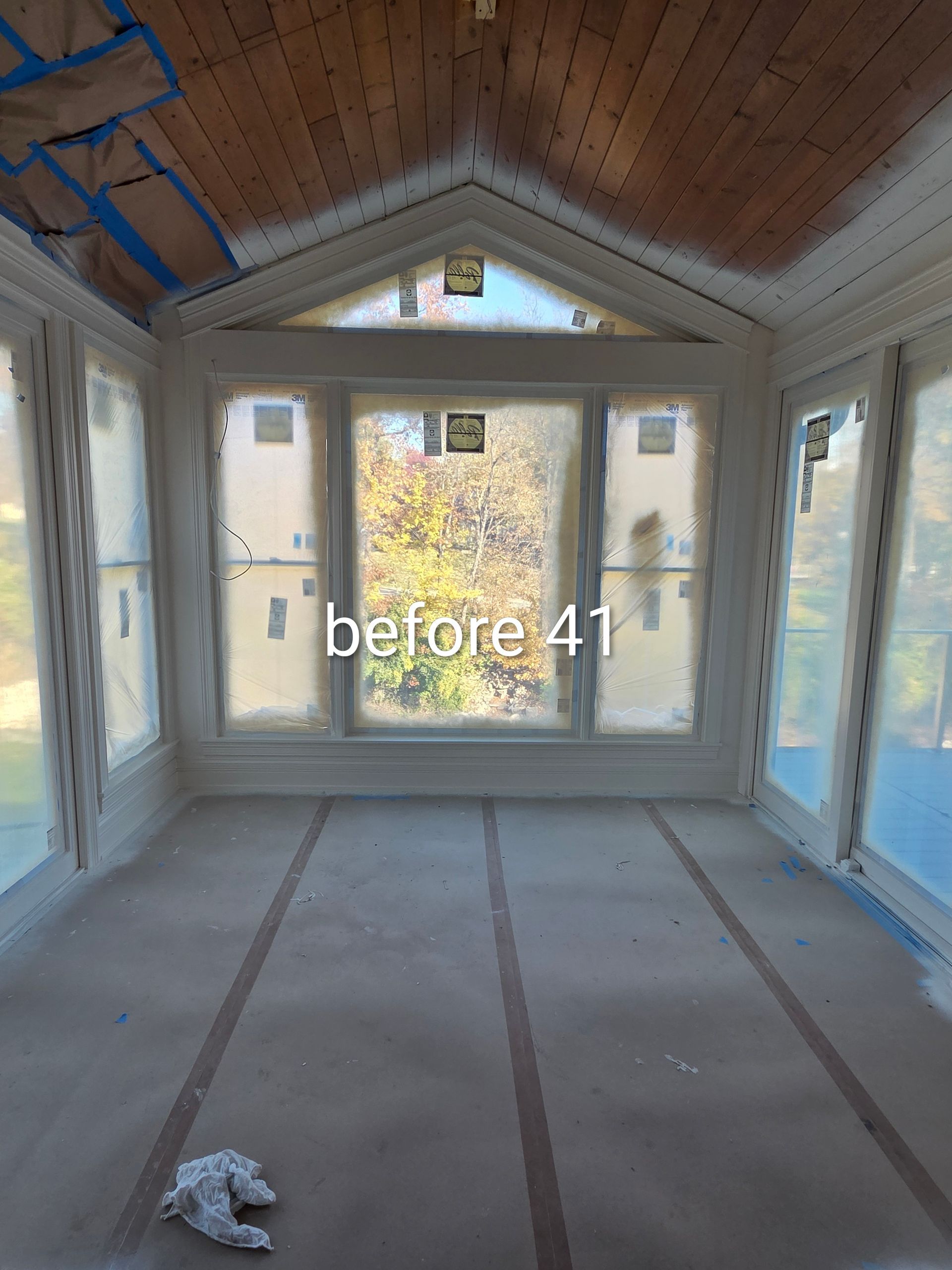 Empty sunroom under construction with unfinished walls, floor, and wood-paneled vaulted ceiling.