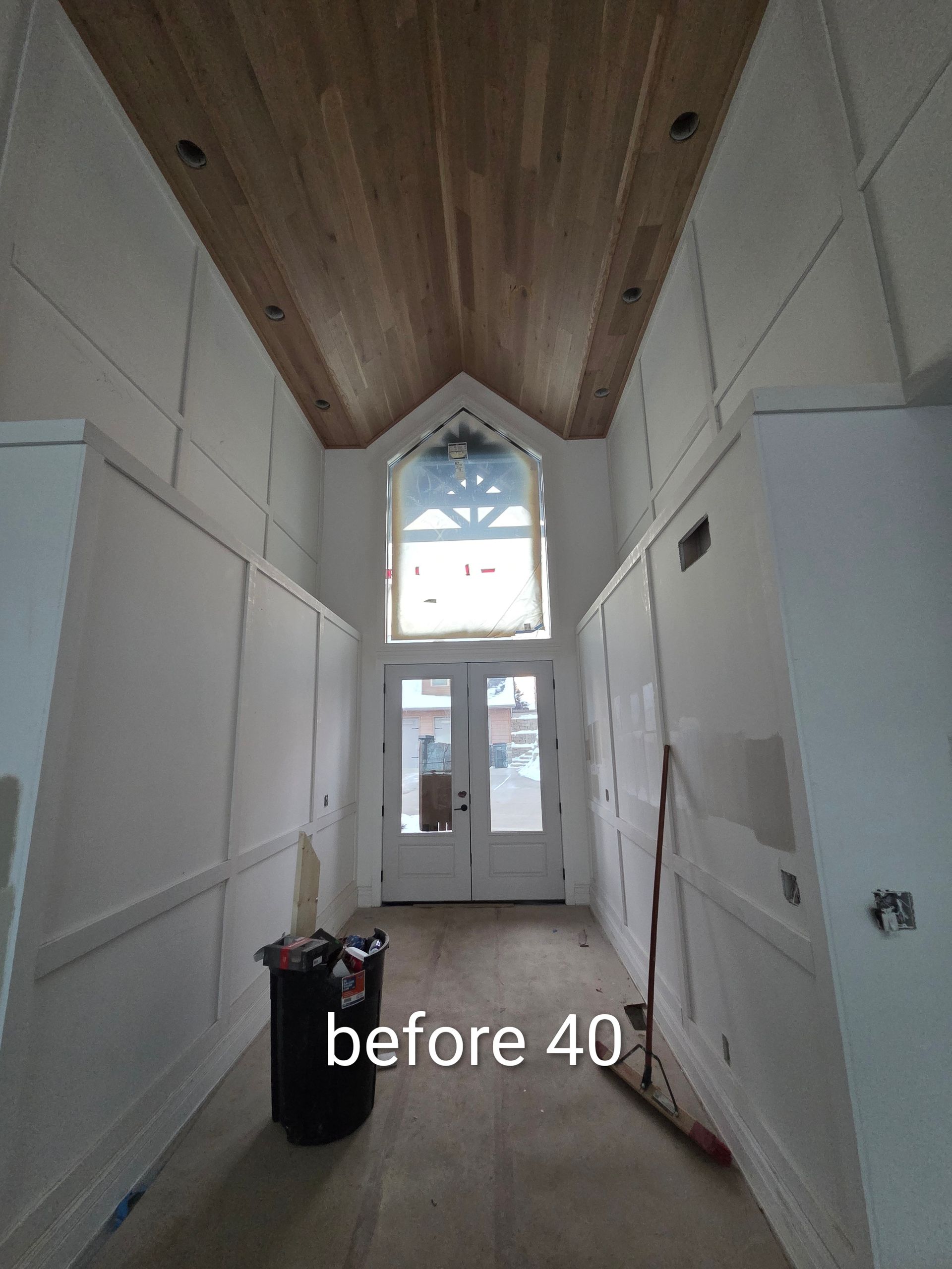 Narrow unfinished hallway with white walls, wood ceiling, and a door with windows at the far end.